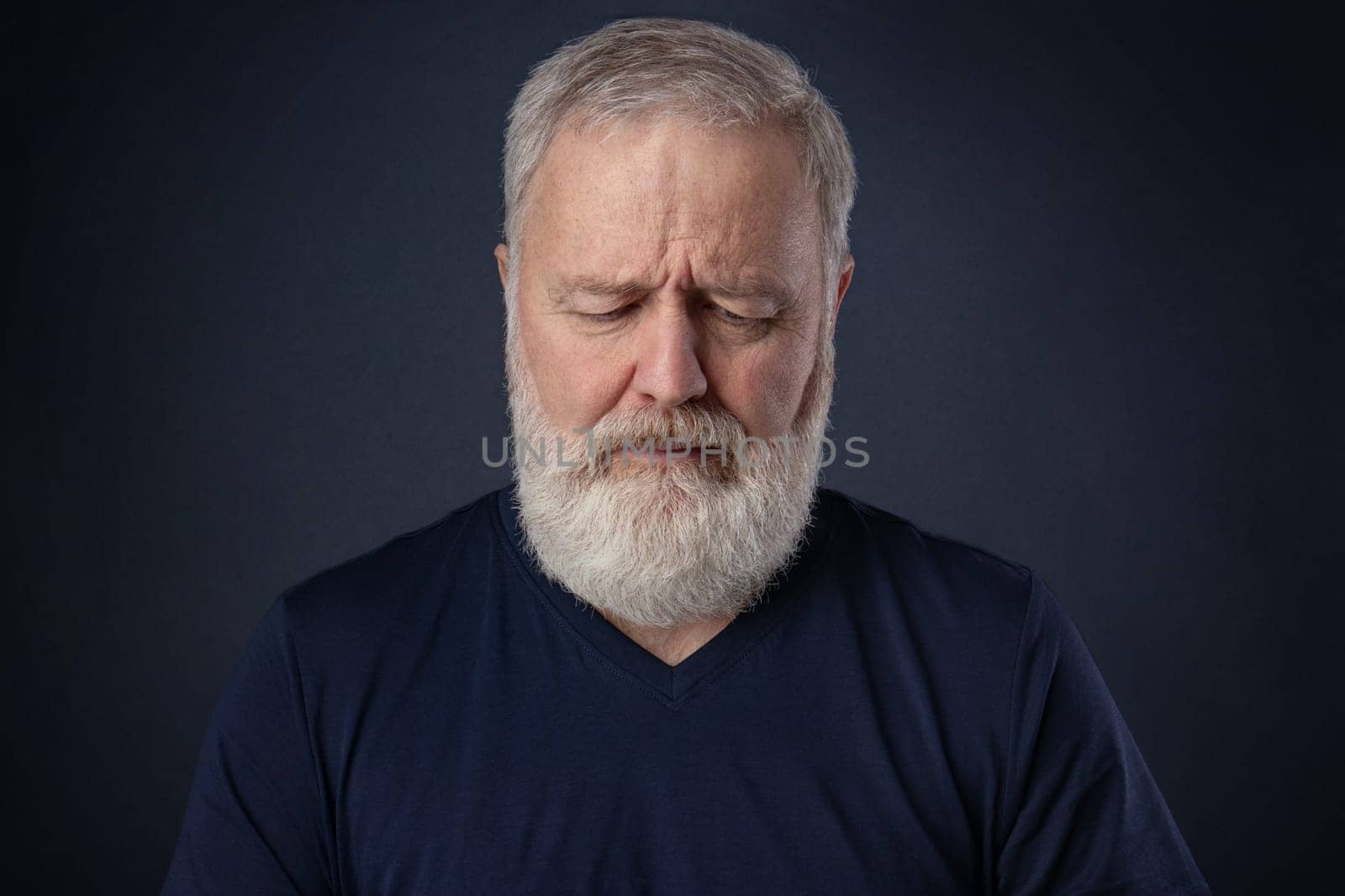 Elderly man with gray beard looking down and thinking
