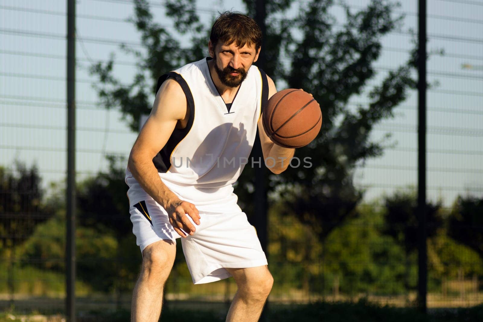 The basketball player is playing basketball or streetball at the street outdoors.