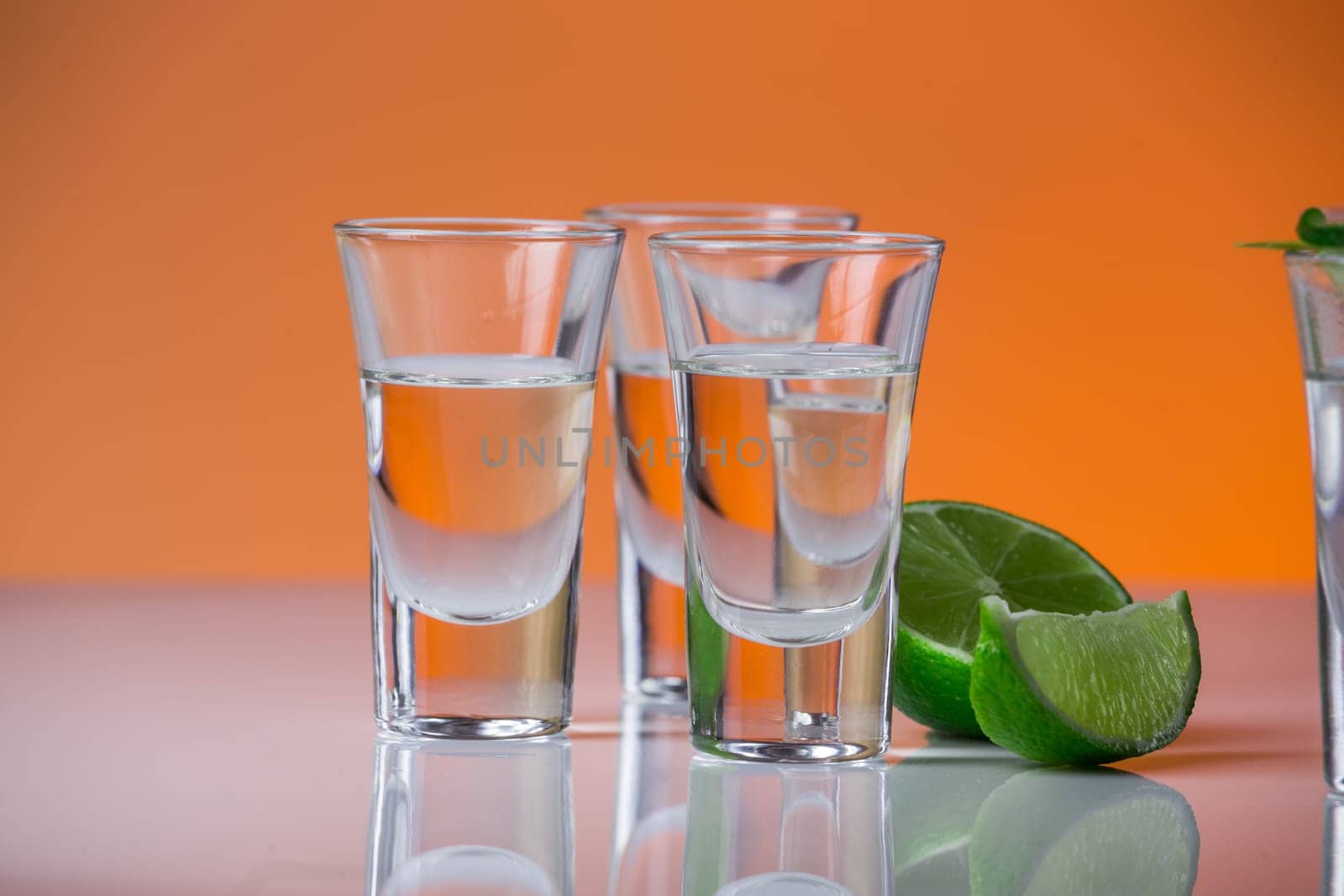 Tequila shot with a slice of lime on the glass on orange background. Selective Focus