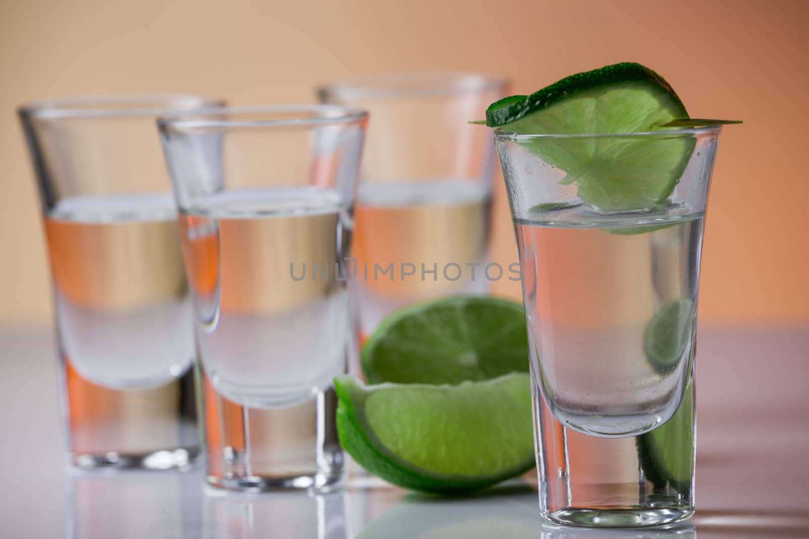 Tequila shot with a slice of lime on the glass on orange background. Selective Focus