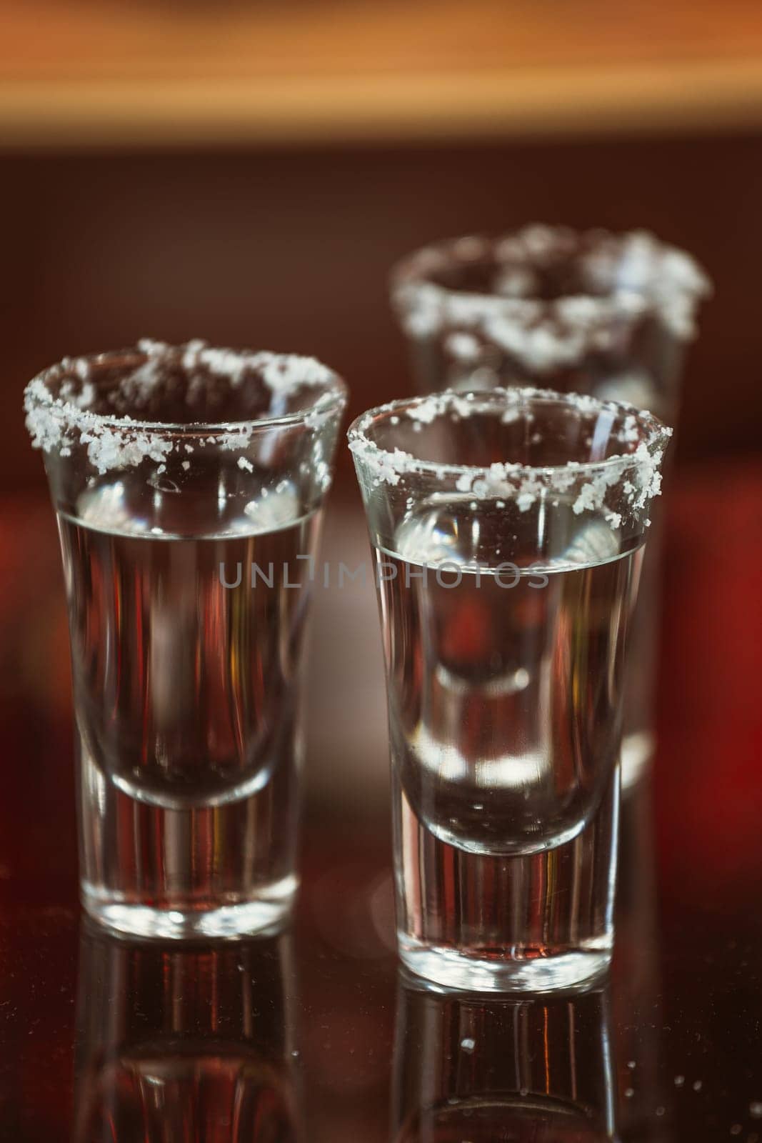 two shots of tequila with lime and salt on a wooden table bar on the background of bright lights of the bar