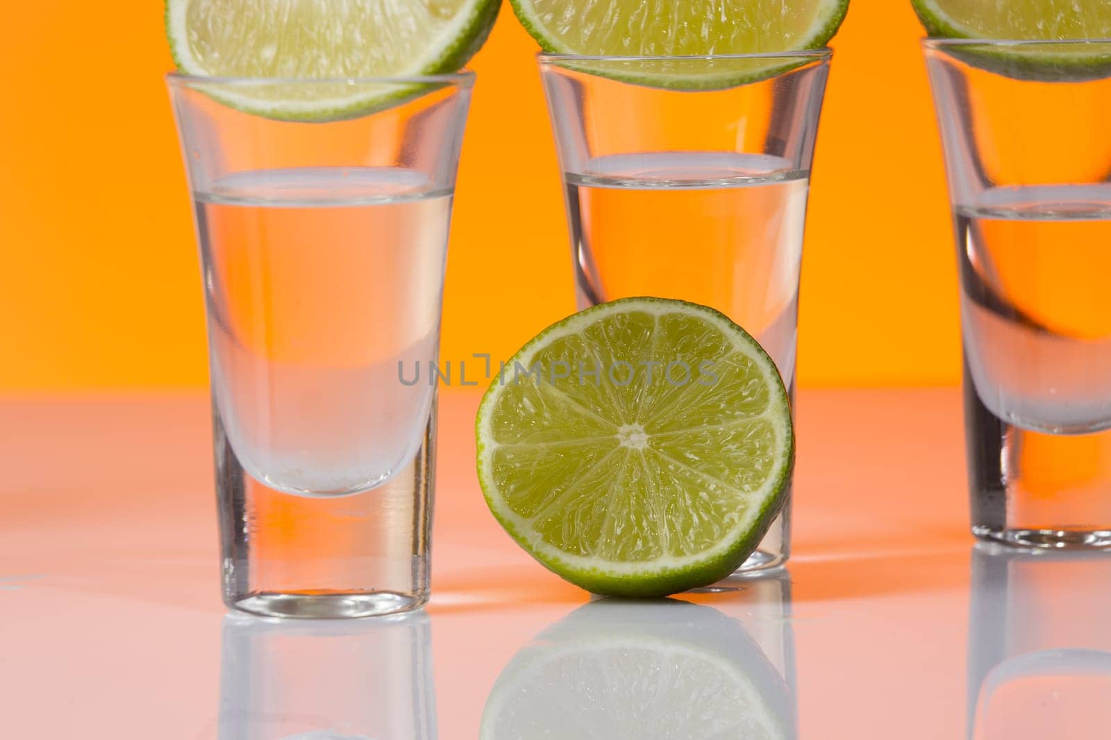 Tequila shot with a slice of lime on the glass on orange background. Selective Focus