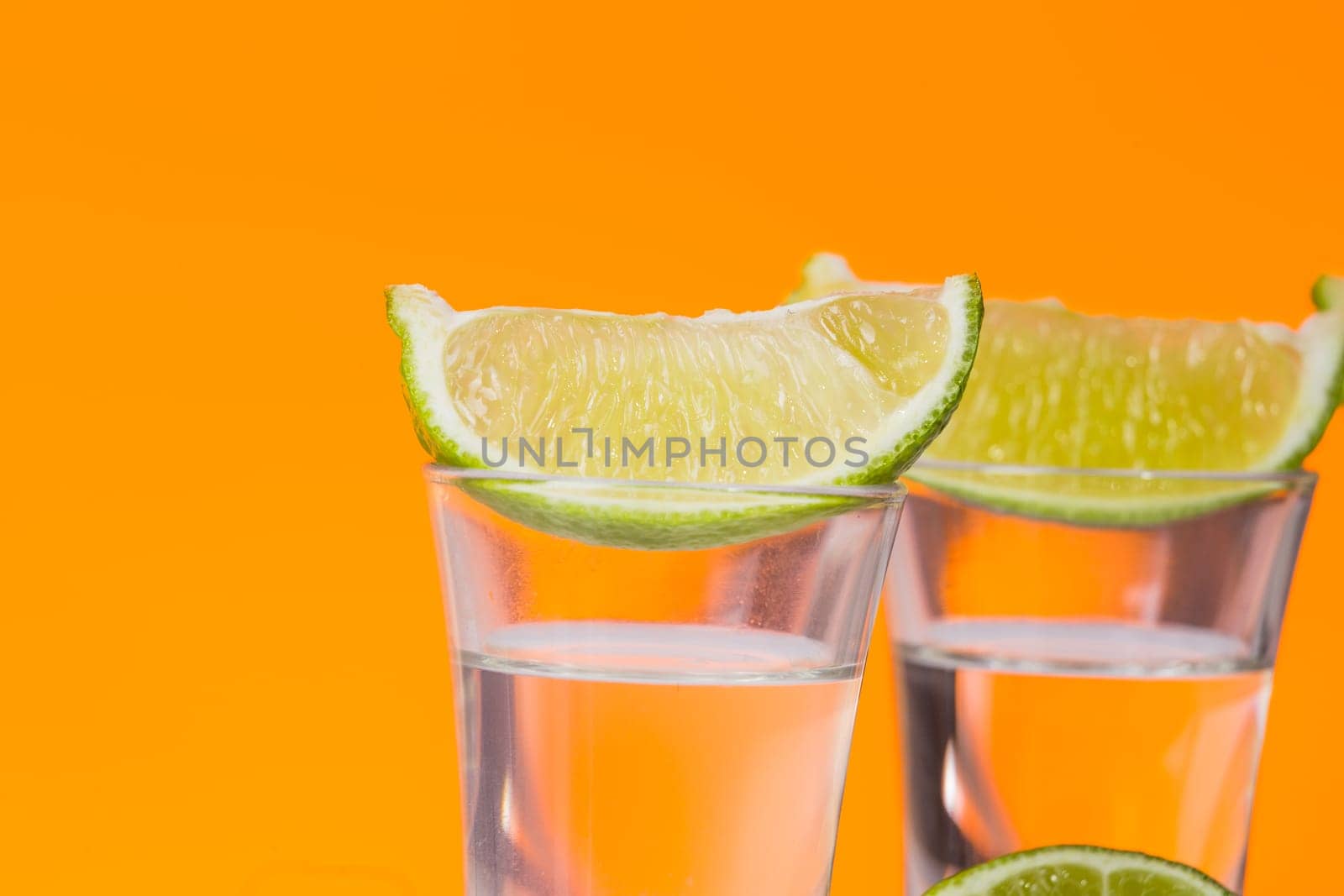 Tequila shot with a slice of lime on the glass on orange background. Selective Focus