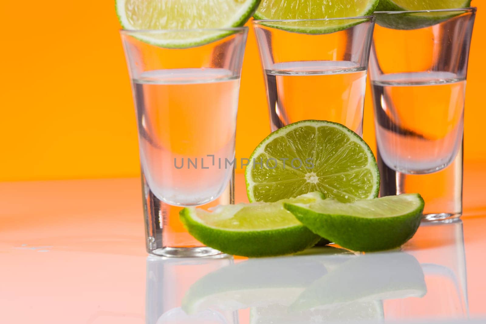 Tequila shot with a slice of lime on the glass on orange background. Selective Focus