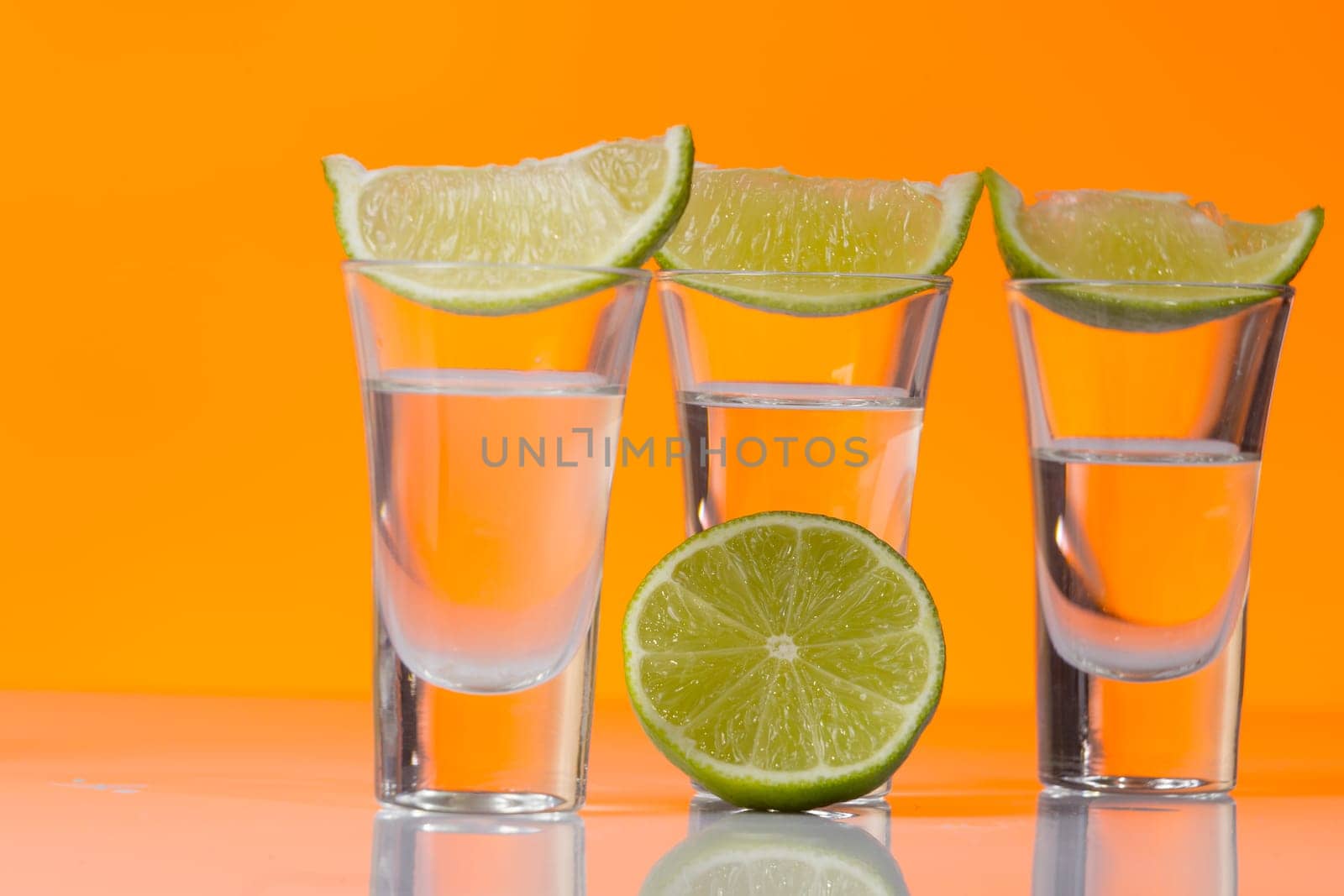 Tequila shot with a slice of lime on the glass on orange background. Selective Focus