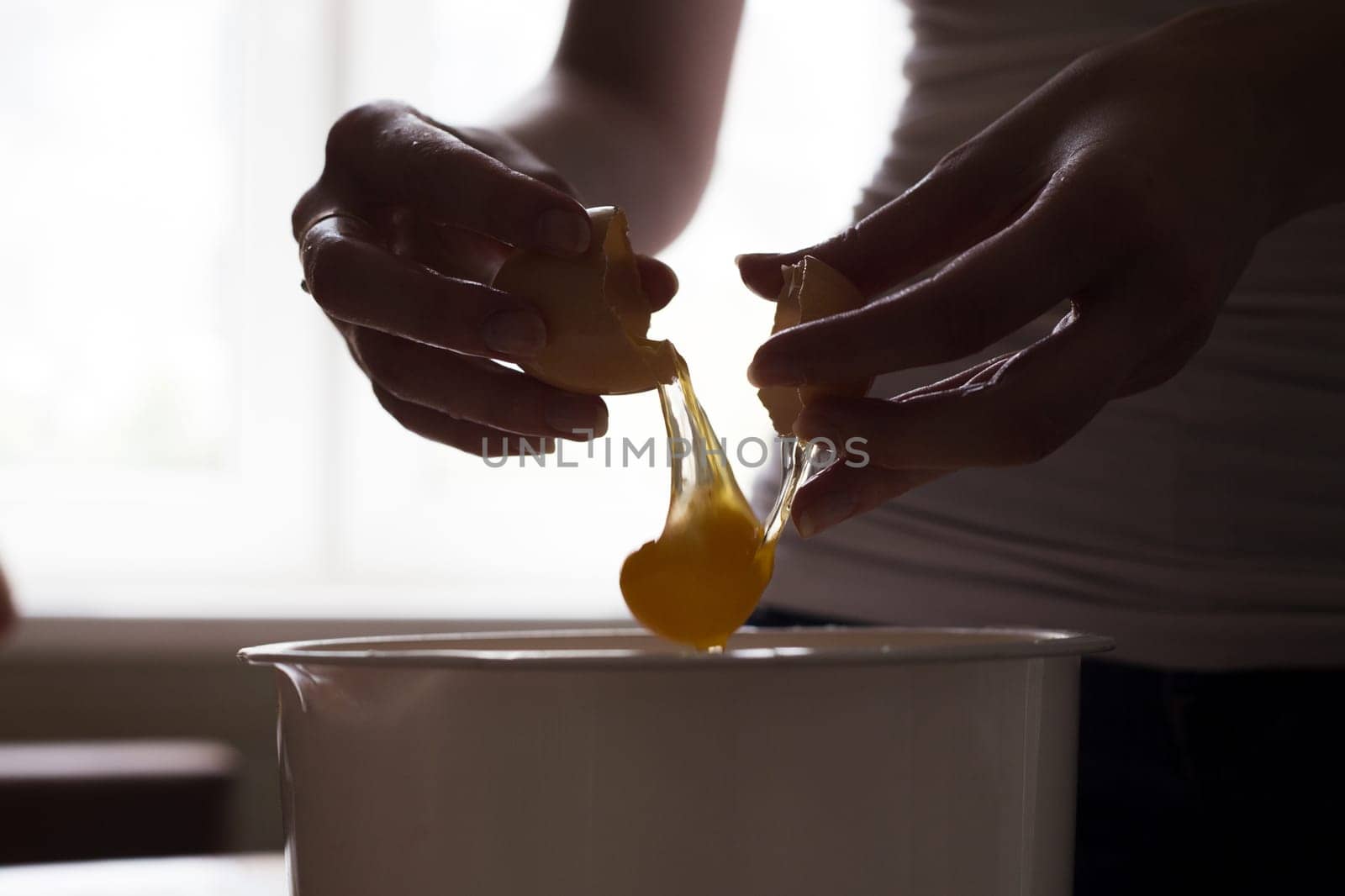 hands opening broken eggshell of brown raw egg