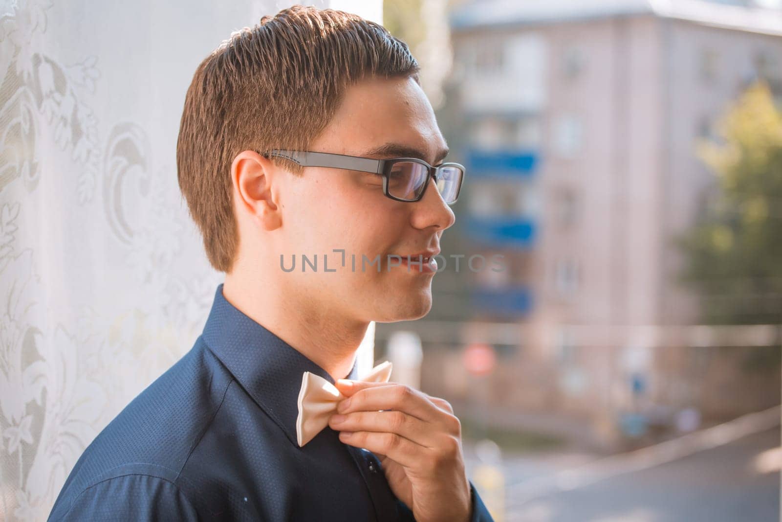 Portrait of young groom tying bow tie while getting ready for wedding