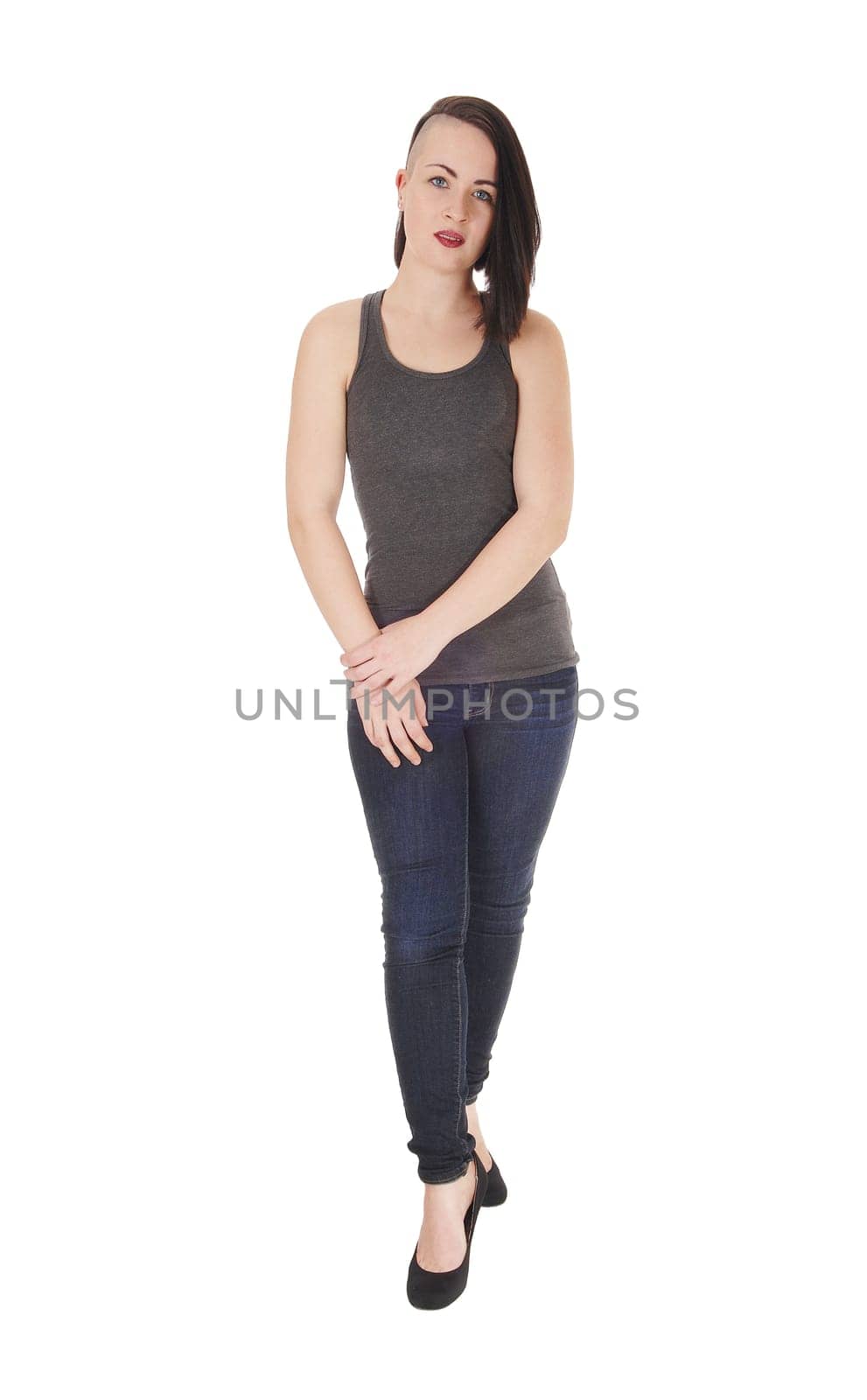 A beautiful young woman standing on white background in jeans and.a t-shirt with short black hair and her hands on her tight.