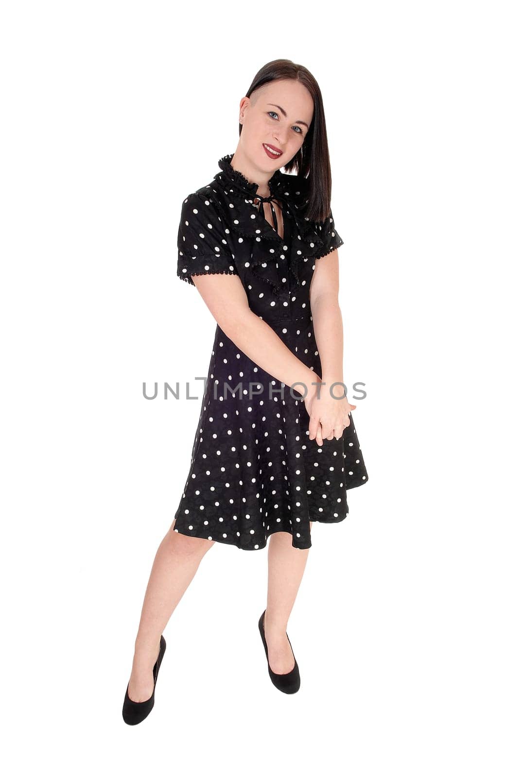 A lovely young woman standing in a pock dot dress from the front in .high heels and short black hair, isolated for white background.