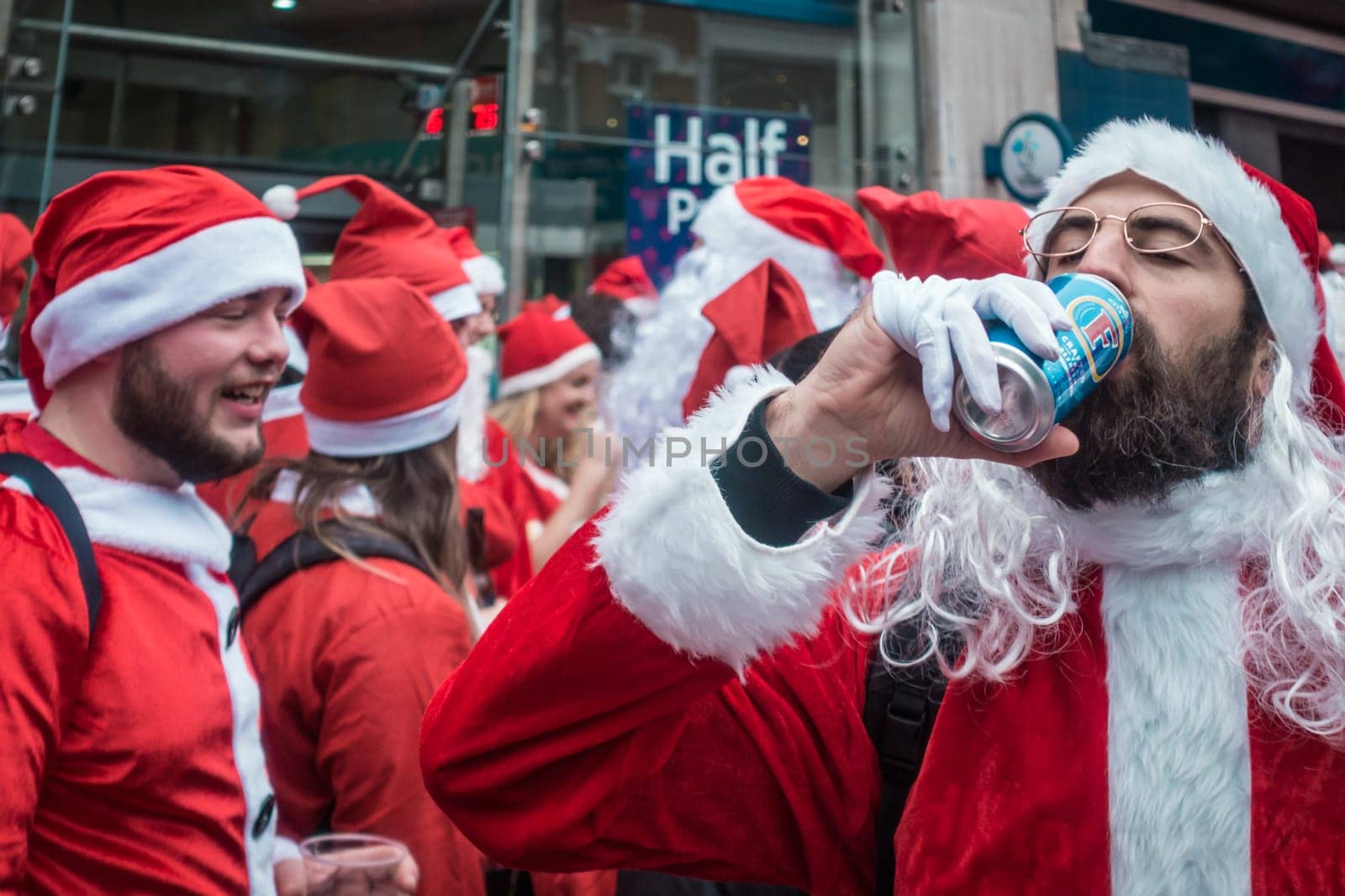 London, UK - December 2018 : Man dressed in santa outfit drinking alcoholic beer from a can while taking part in a themed SantaCon event