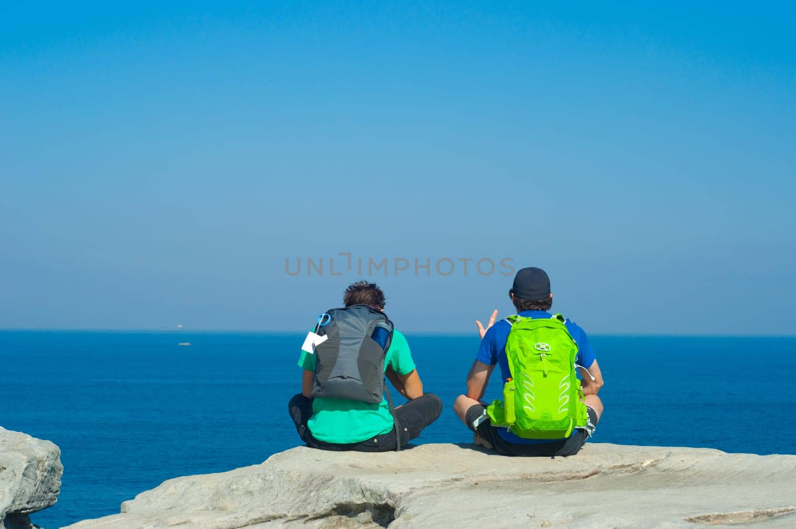 Portrait from behind of young men sitting and looking on Sea with backpack. Concept for travel or freedom.