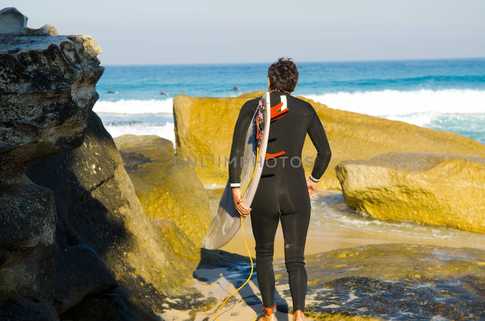 Professional surfer carrying his surfboard while going to the sea, professional surfer in black diving suits ready to surf walk to the ocean.