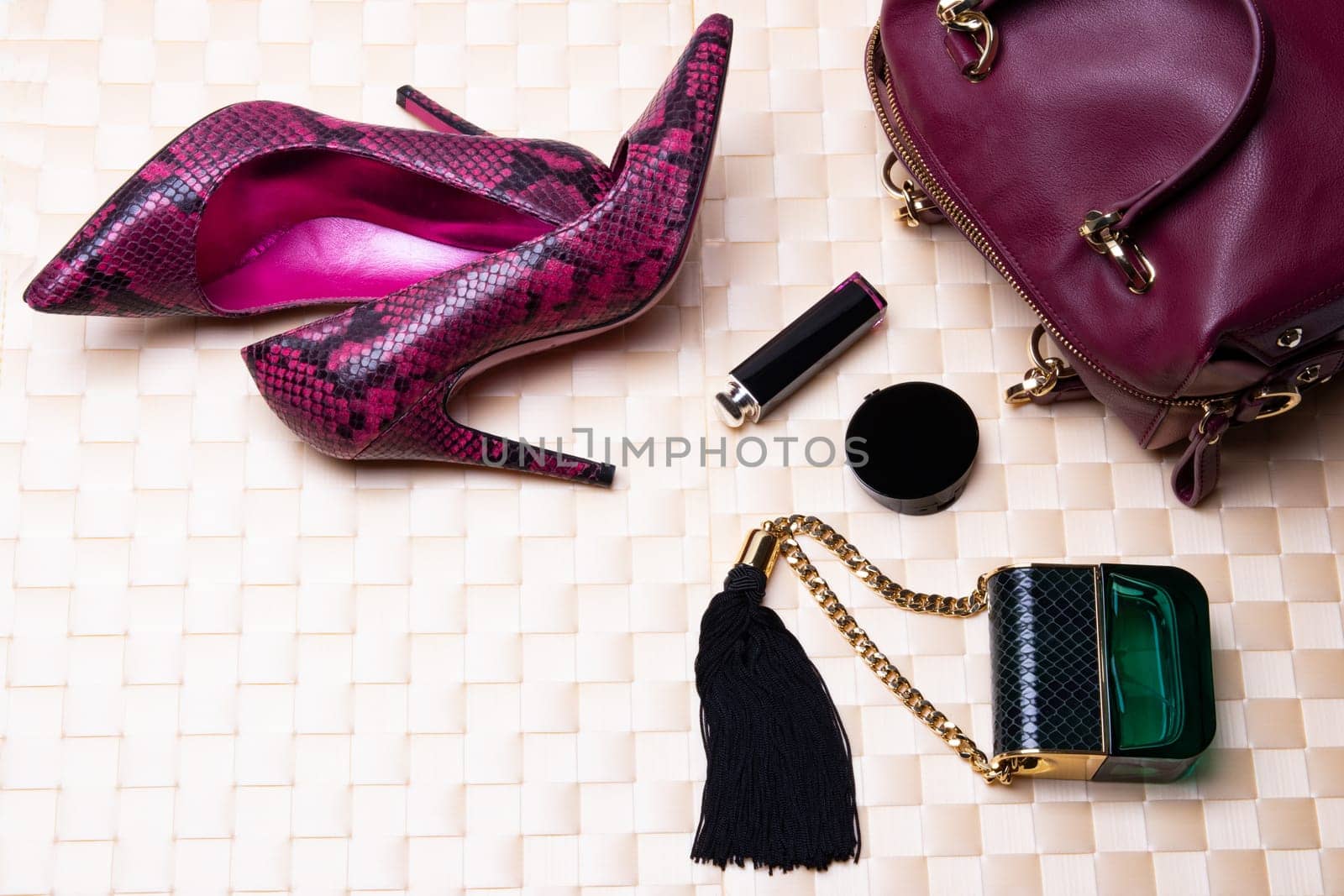 Top view to flat lay fashionable high heels, leather handbag, perfume and cosmetics on a bright table cloth.