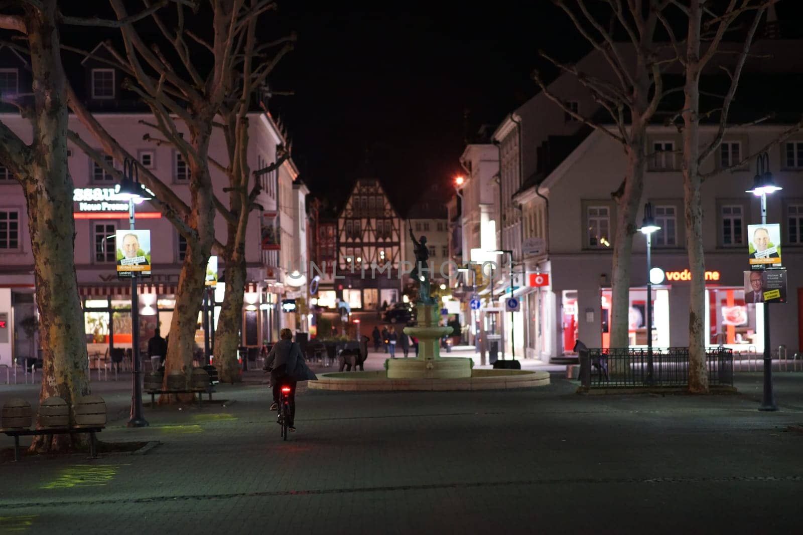 Limburg, Germany - November 03, 2018: A cyclist driving through the city center of Limburg at night with illuminated shops on November 03, 2018 in Limburg..