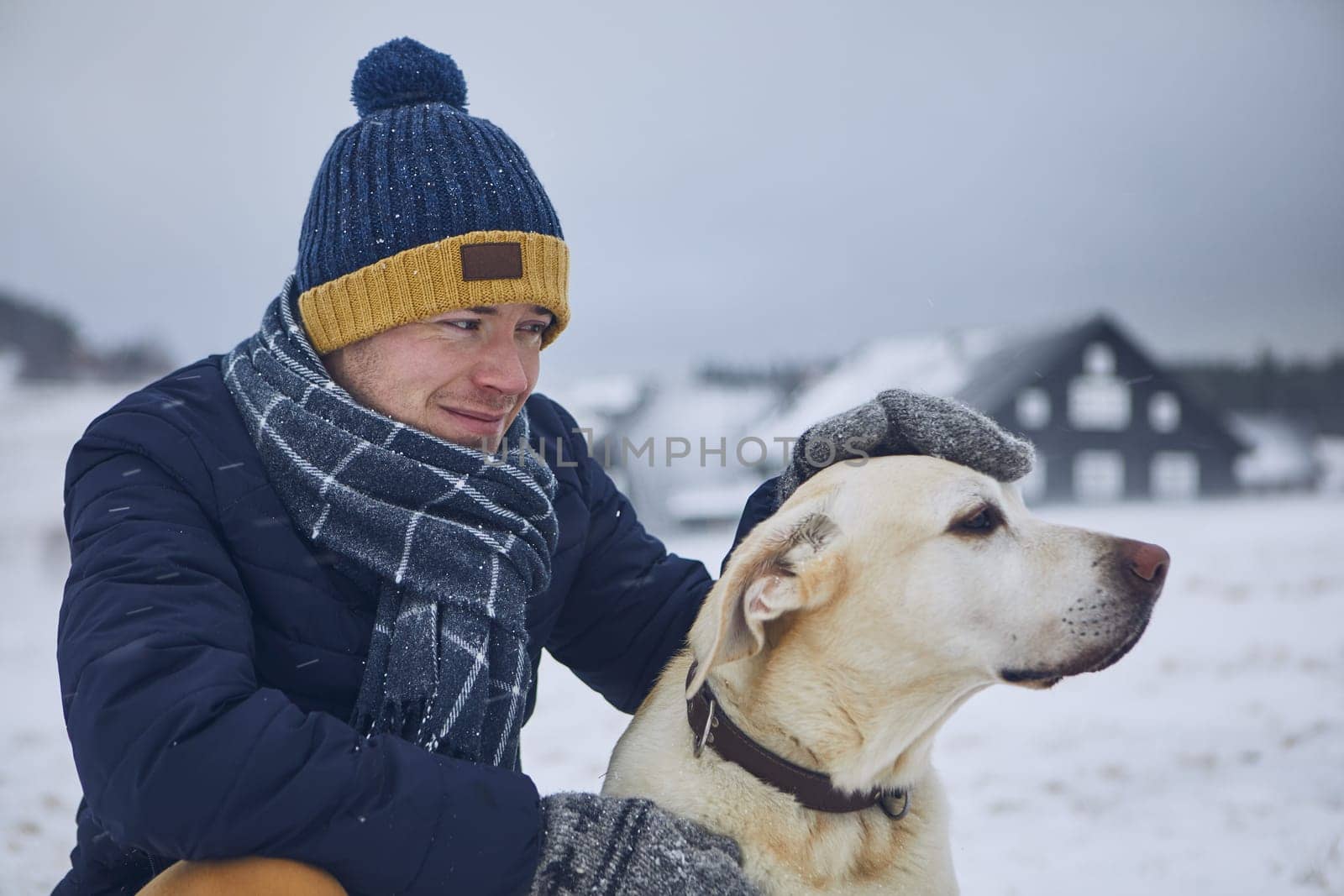 Friendship between pet owner and his dog. Young man stroking labrador retriver in winter landscape.
