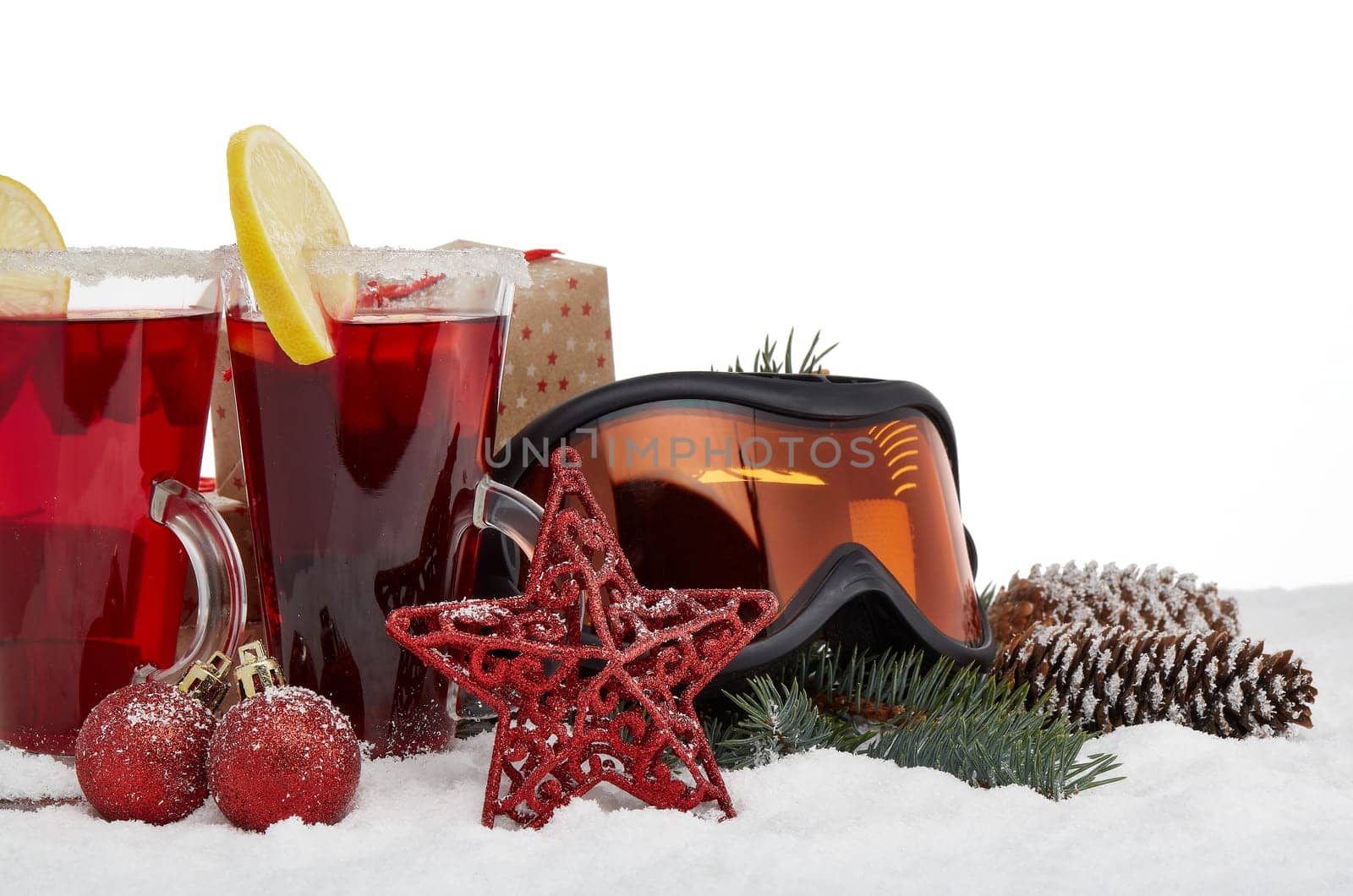 Winter holidays still life with gift boxes, fir tree branch, ski glasses, mulled wine and Christmas decorations on snow on a white background with copy space. New Year and Christmas. Winter vacation.
