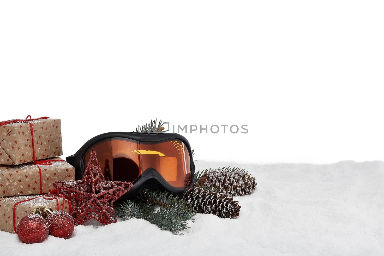 Winter holidays still life with gift boxes, fir tree branch, ski glasses and Christmas decorations lying on snow on a white background with copy space. New Year and Christmas. Winter vacation.