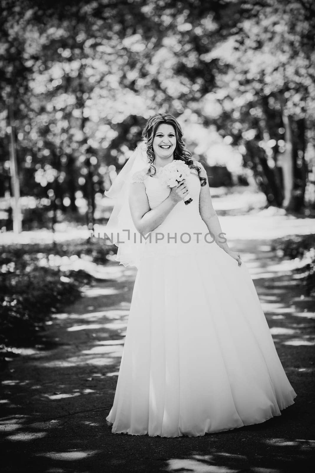 Black white photography stylish beautiful happy bride holding bouquet of flowers on a background of trees in the summer park close-up