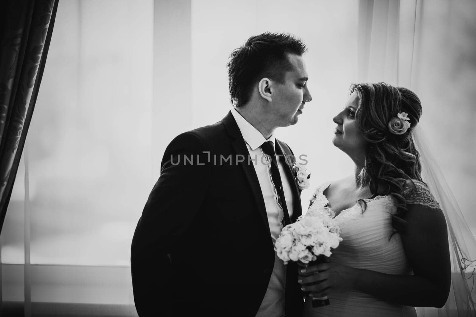 Black white photography bride and groom posing in a hotel room on background windows