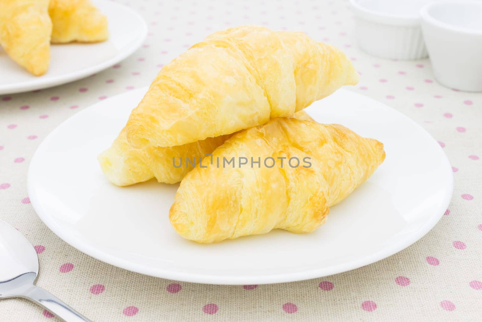 Croissant or Bakery or bread on white dish on pink point placemat with spoon and tea cup