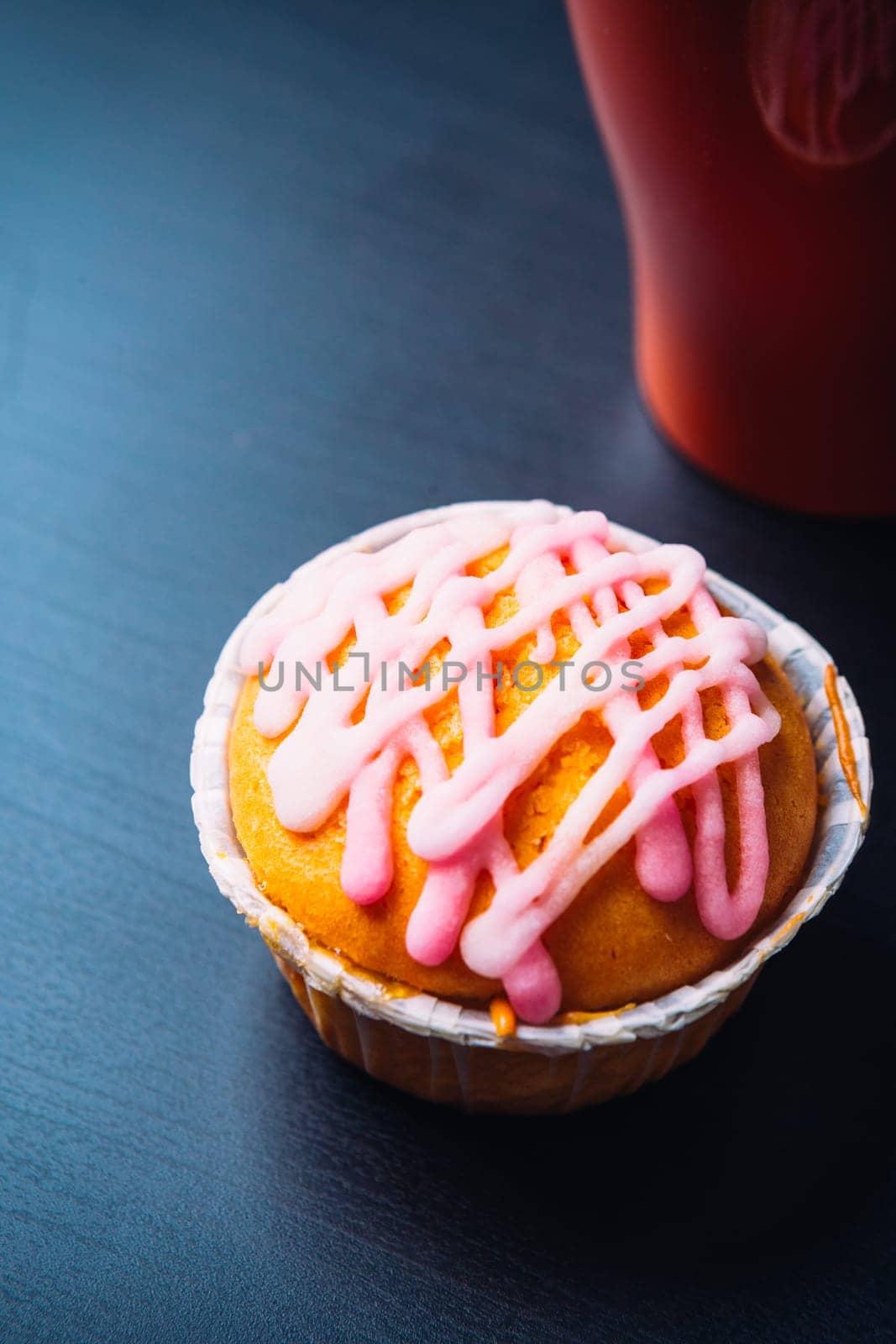 cupcake with pink frosting and red cup on a wooden background