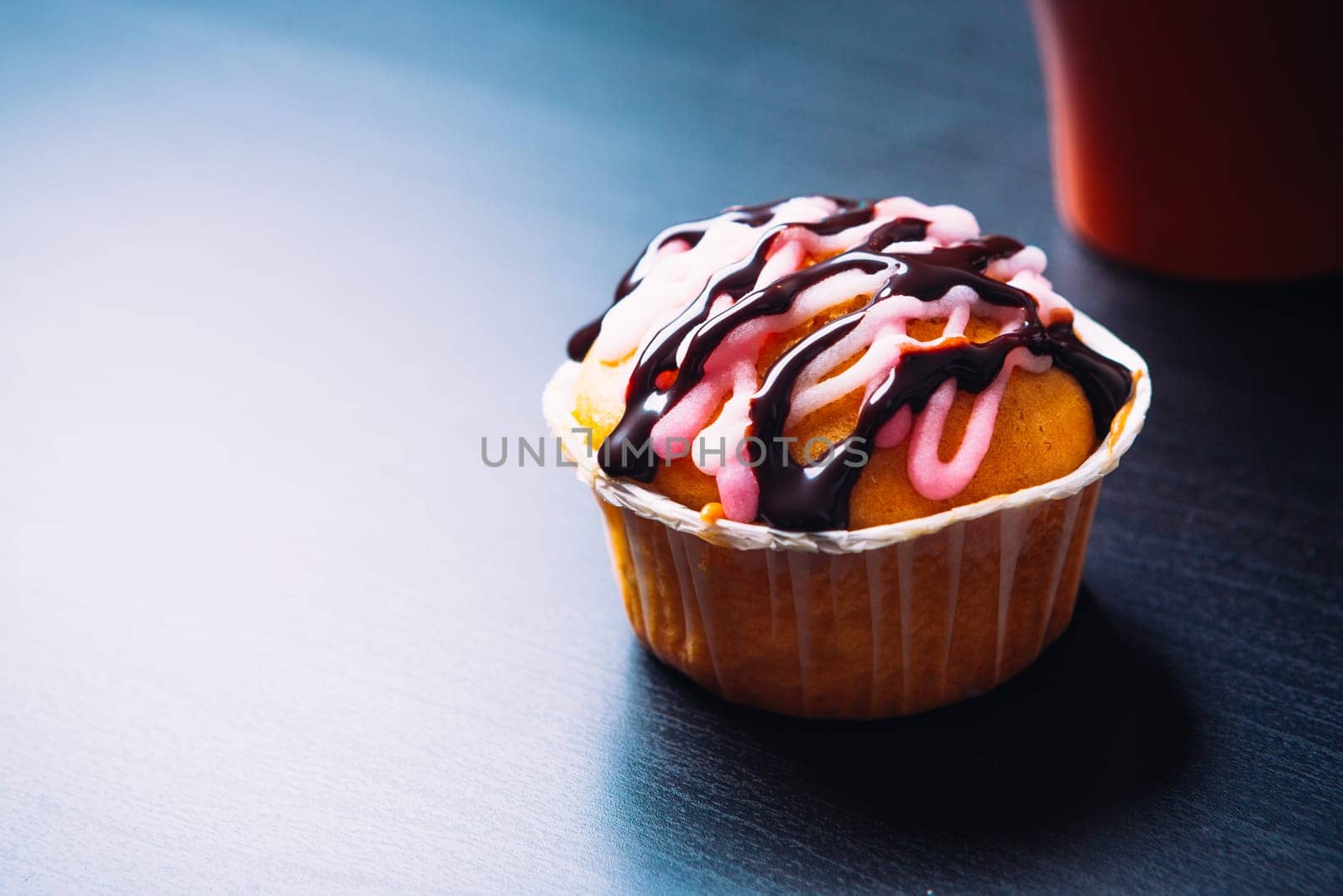 cupcake with pink frosting and red cup on a wooden background