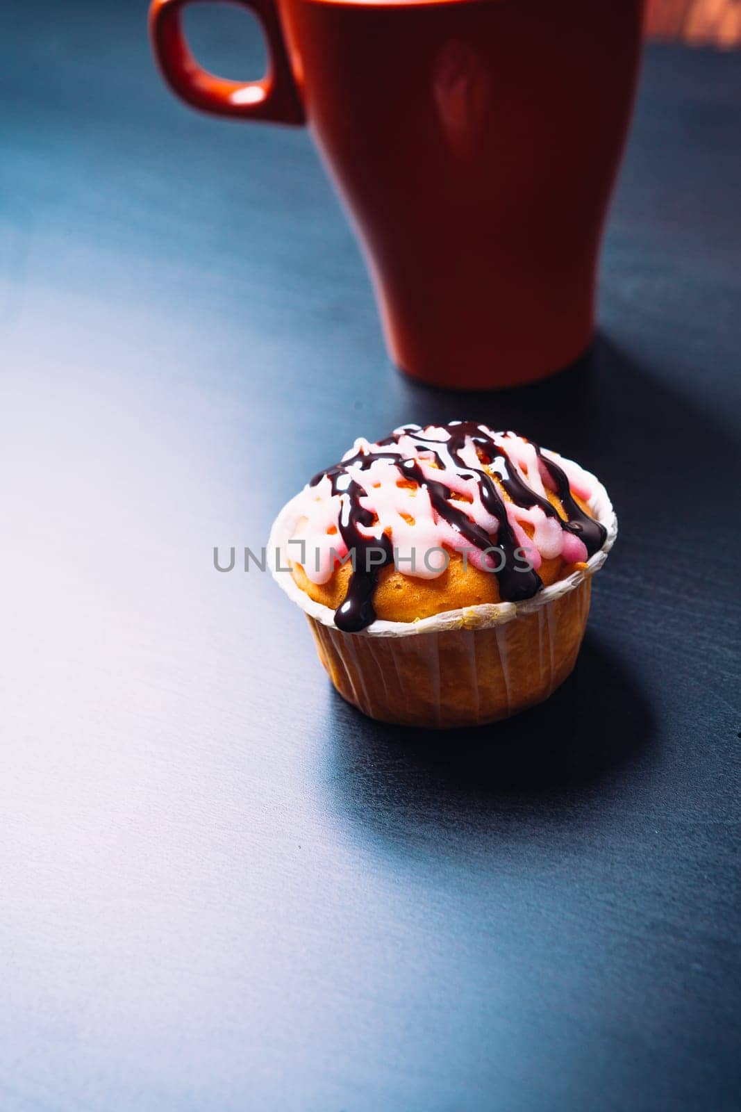 cupcake with pink frosting and red cup on a wooden background