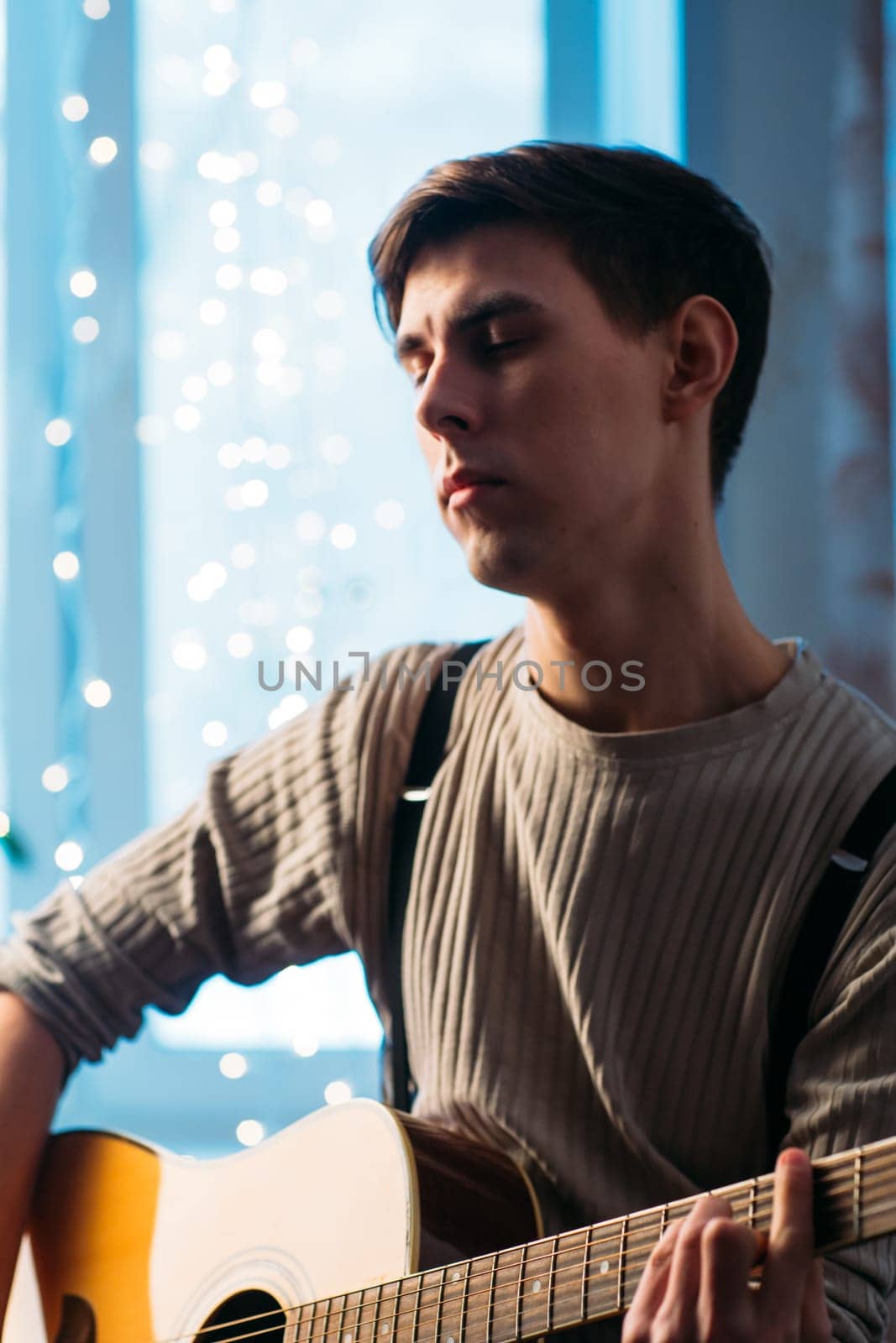 Young man sitting at home and playing guitar dramatic