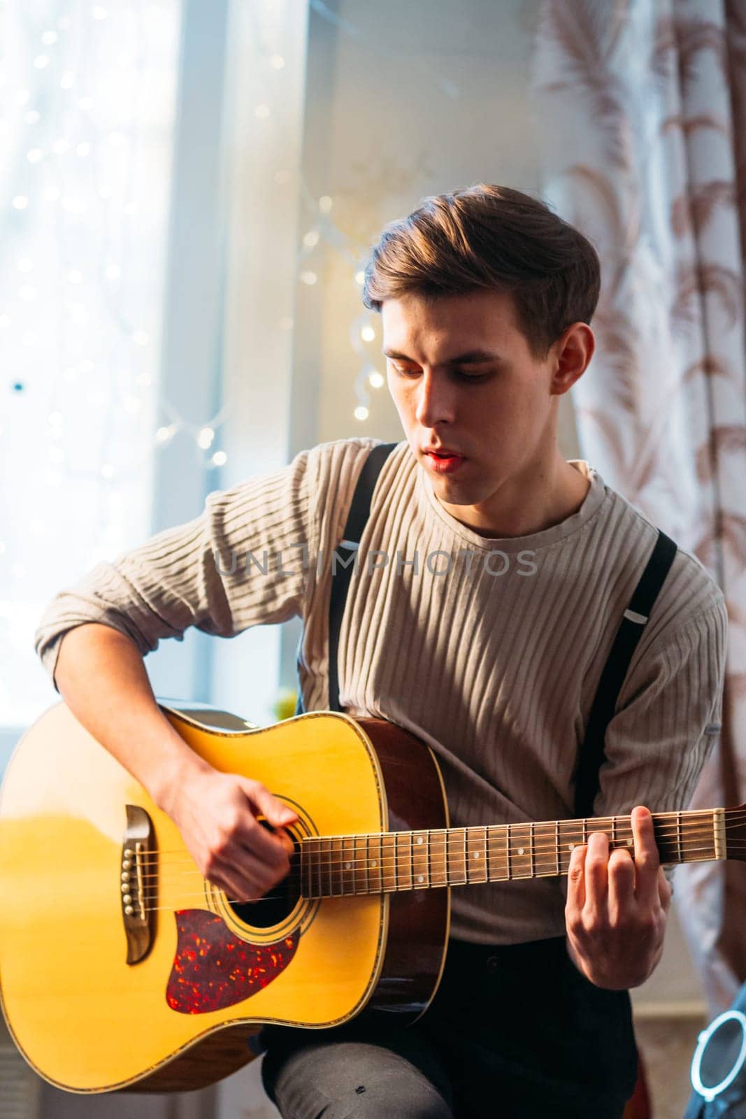 Young man sitting at home and playing guitar dramatic