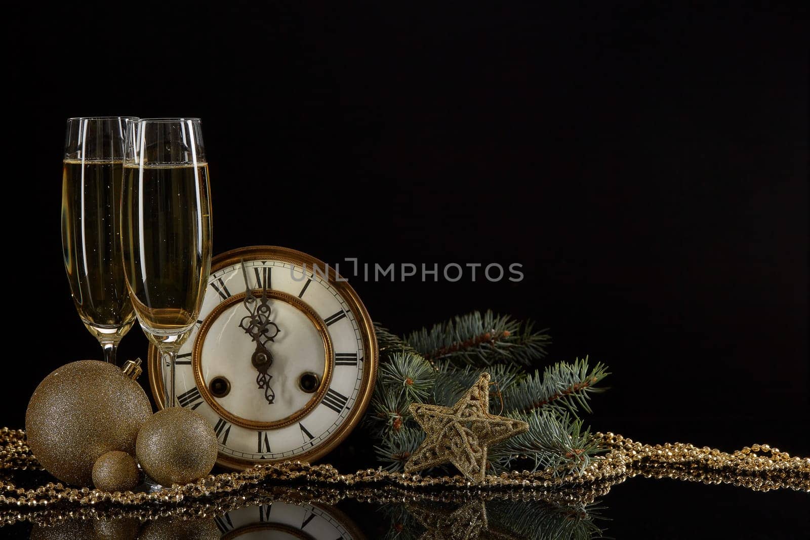 Two wineglasses with champange, bottle, gift box, clock and christmas ornament on a black background with reflection. Copy space. Christmas and New Year background