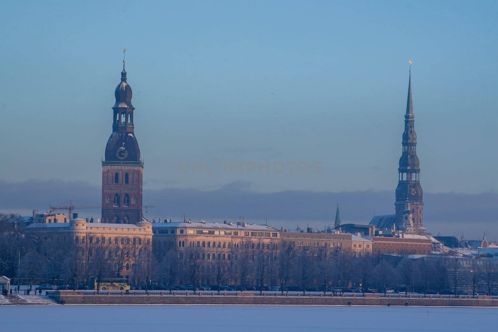 Riga view in winter. Riga, capital city of Latvia in winter time. View of St Peter's Church and St. Jacob's Cathedral. View of Old Riga with frozen river Daugava in the foreground. City Riga with background of blue sky.