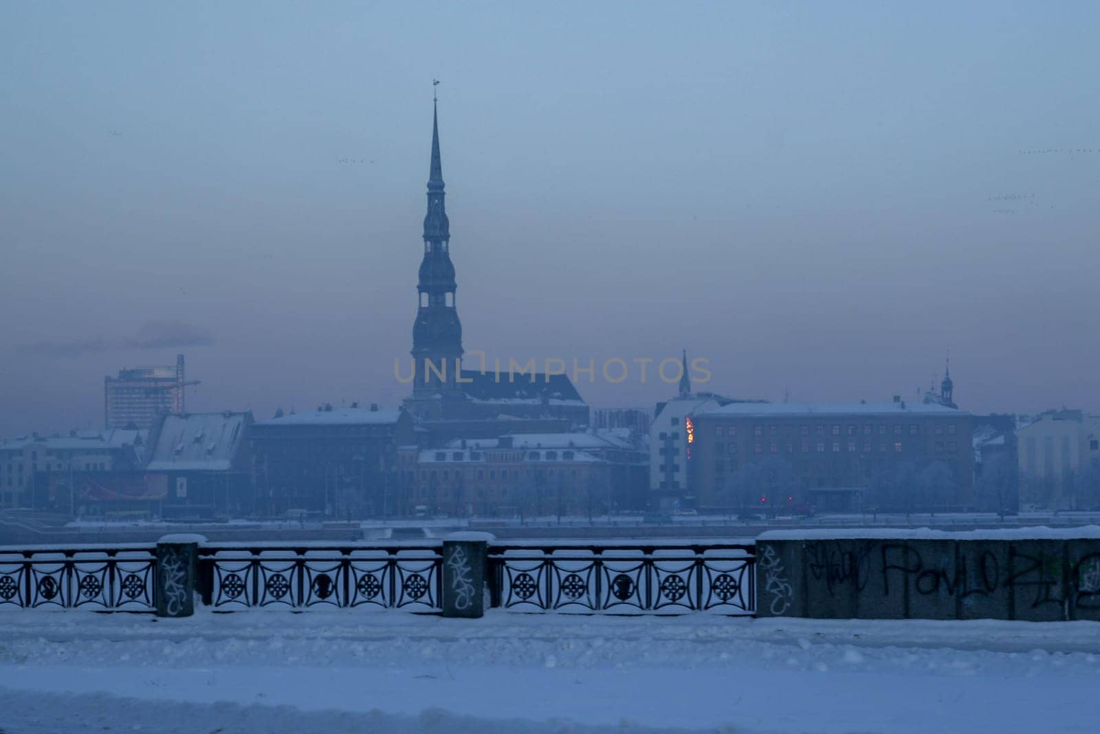 Riga view in winter  Riga, capital city of Latvia in winter time. View of St Peter's Church in winter. View of Old Riga with frozen river Daugava in the foreground. City Riga with background of blue sky.