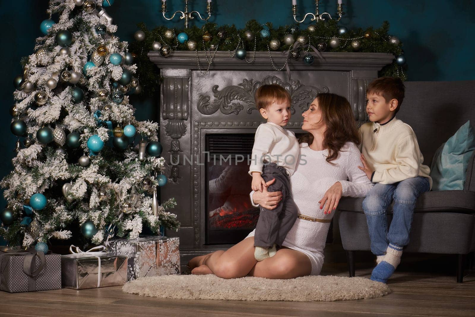 Happy family are sitting near Christmas tree at home. Merry Christmas and Happy New Year. Beautiful young mother with two sons.
