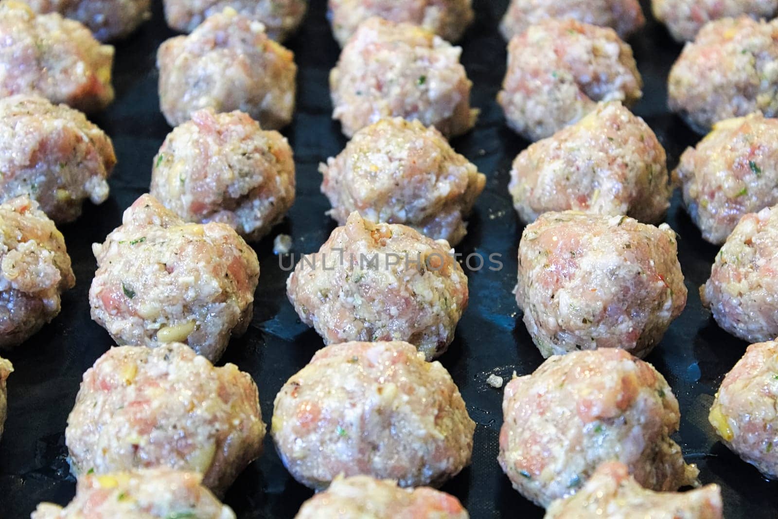 Raw turkey meatballs on a black cooking sheet.