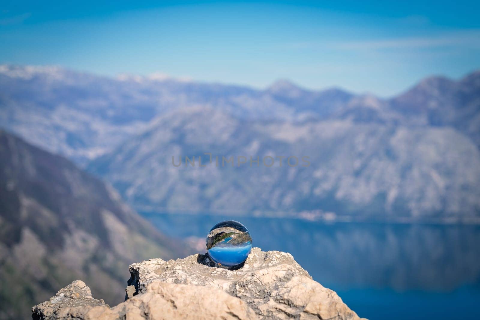 Stunning landscape of the Bay of Kotor and Lovcen National Park in Montenegro reflected in a large glass ball placed on a large boulder