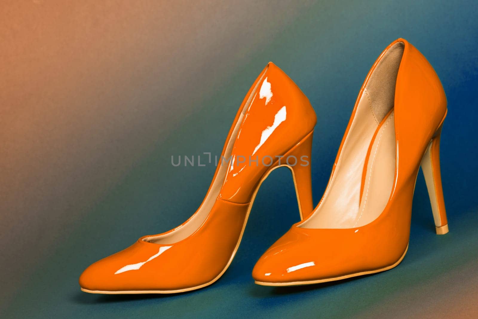 The sexy orange high heels shoes are on blue and orange background.