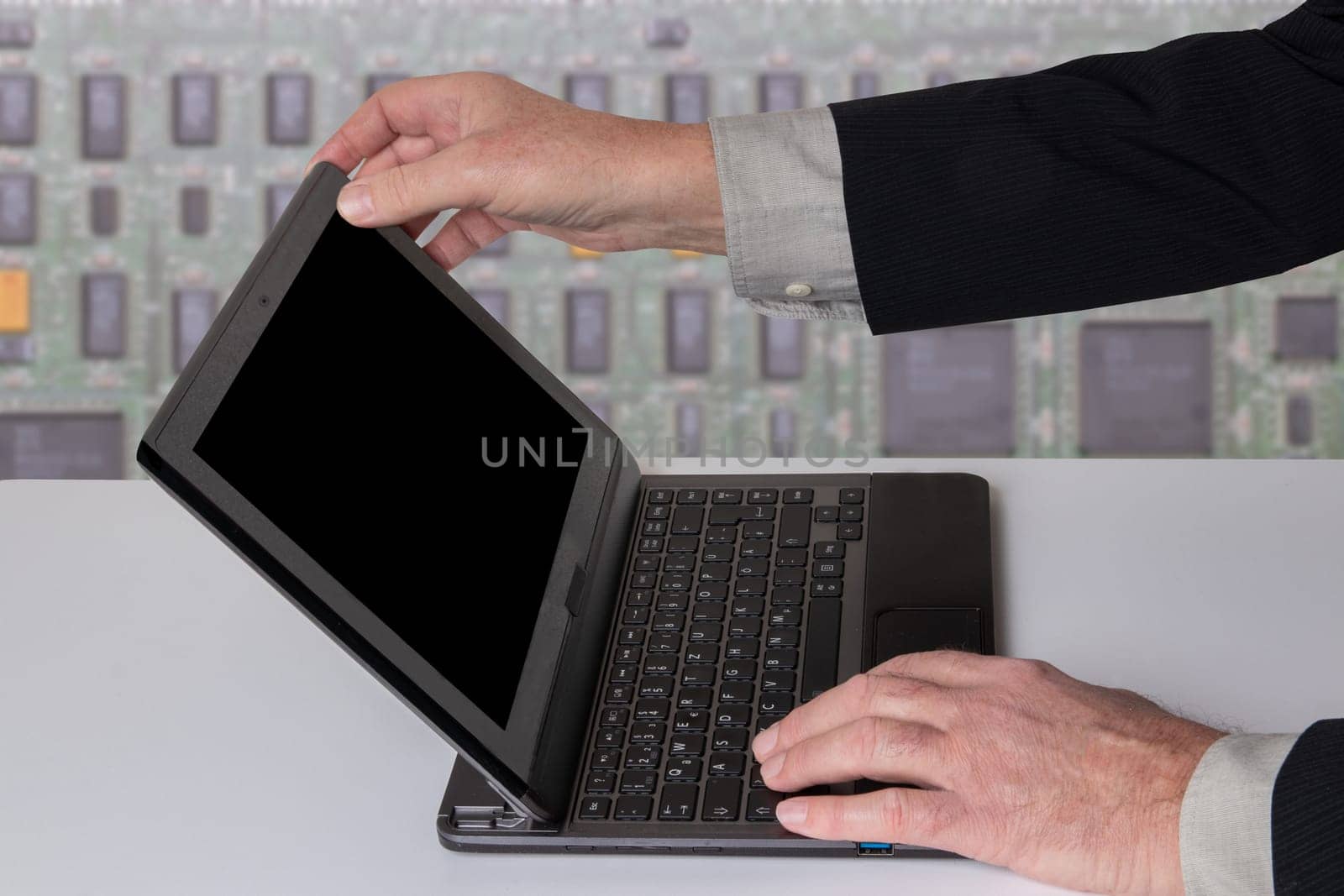 Hands of a unrecognizeable businessman working with a modern portable computer on a white table. Computer in front of abstract bright technology background.
