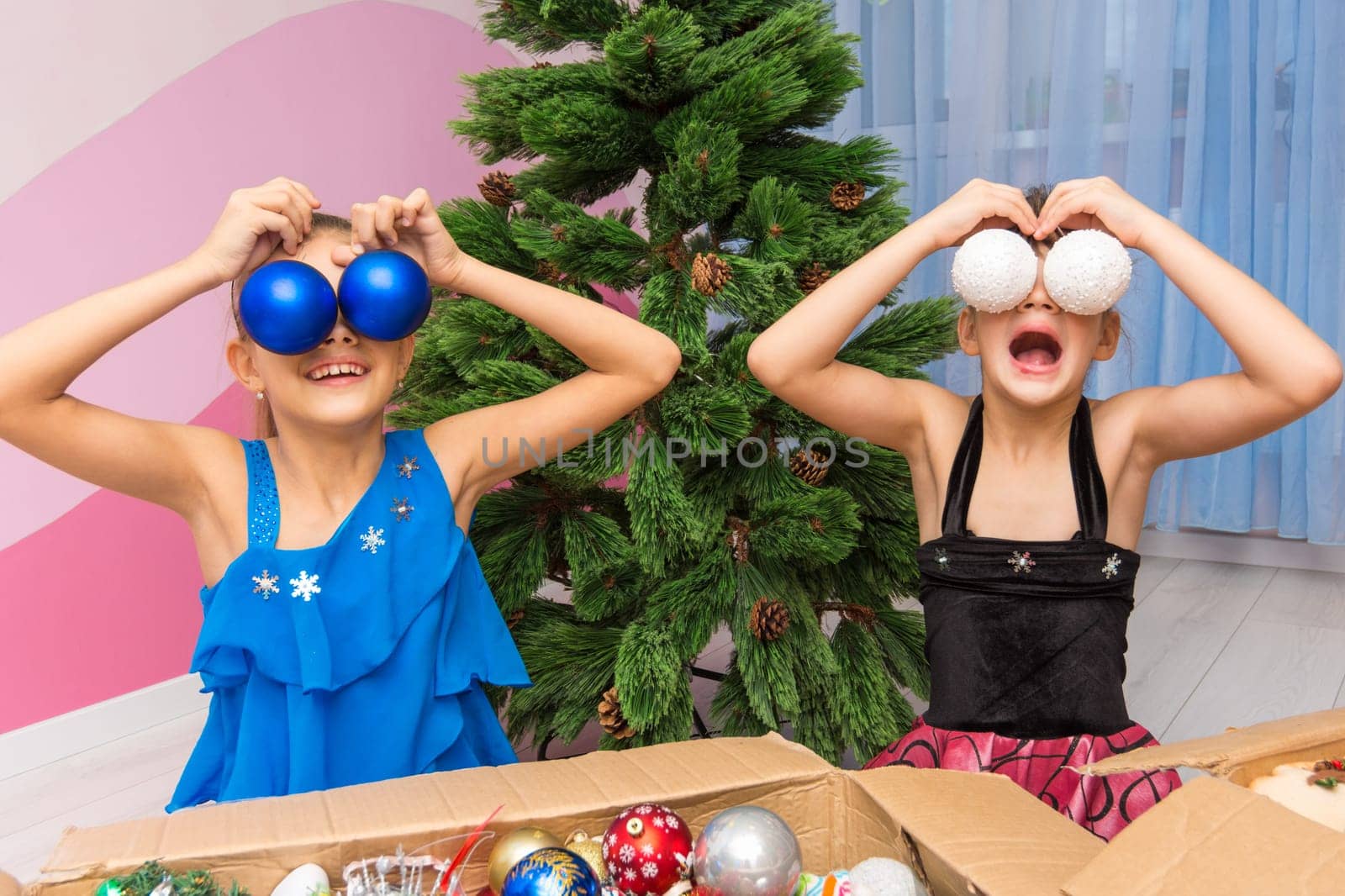 Two girls put big Christmas balls to their eyes