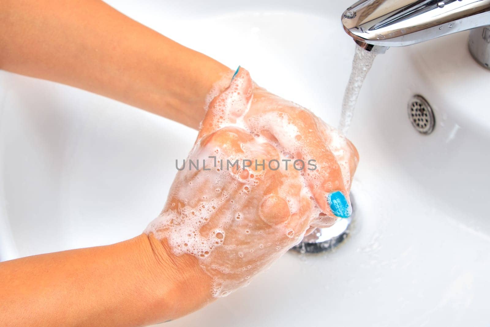 Female hands under running water in the sink