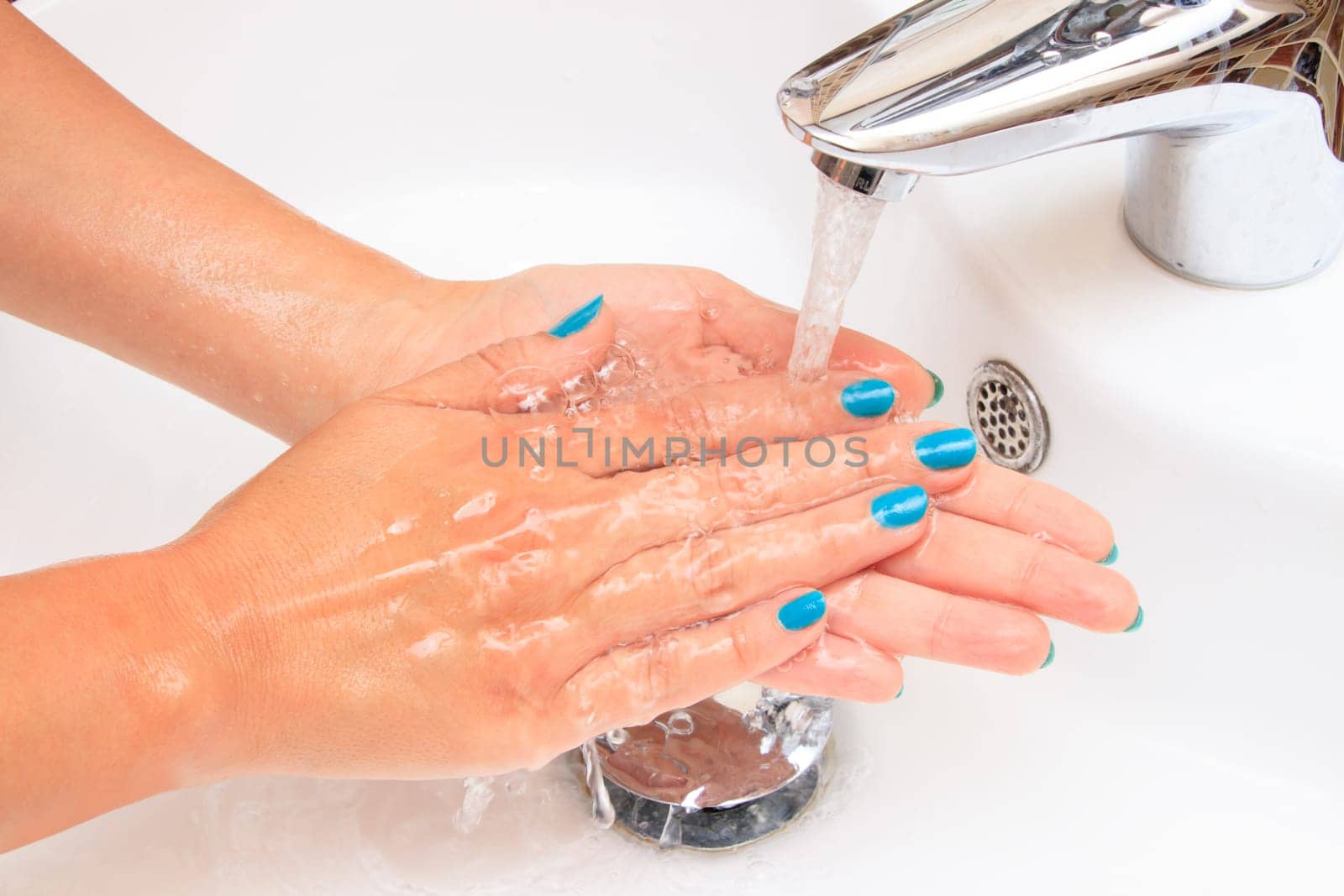 Female hands under running water in the sink