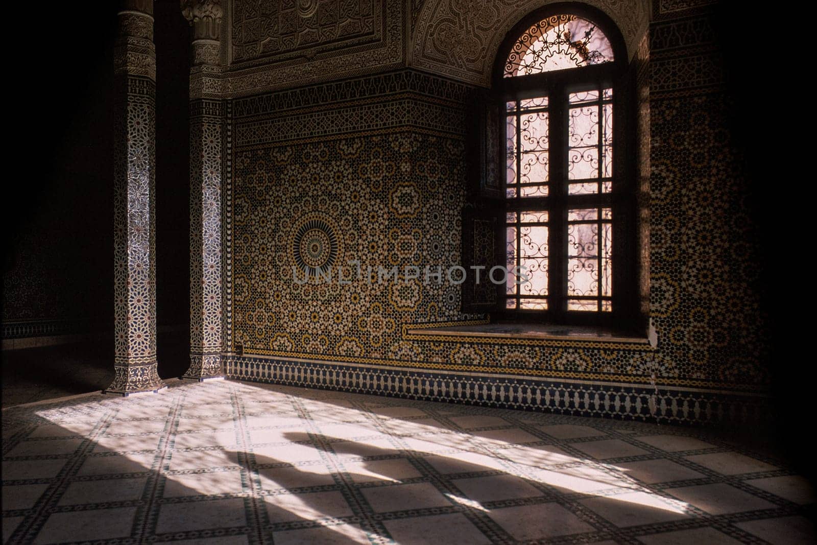 Horizontal image with partial view of a magnificent interior, a facade decorated with stucco and tile mosaics. A window with ornaments and two shadows that appear at the entrance to the room. Kasbah of Pasha Glaoui, in Telouet, Ouarzazate, Morocco.