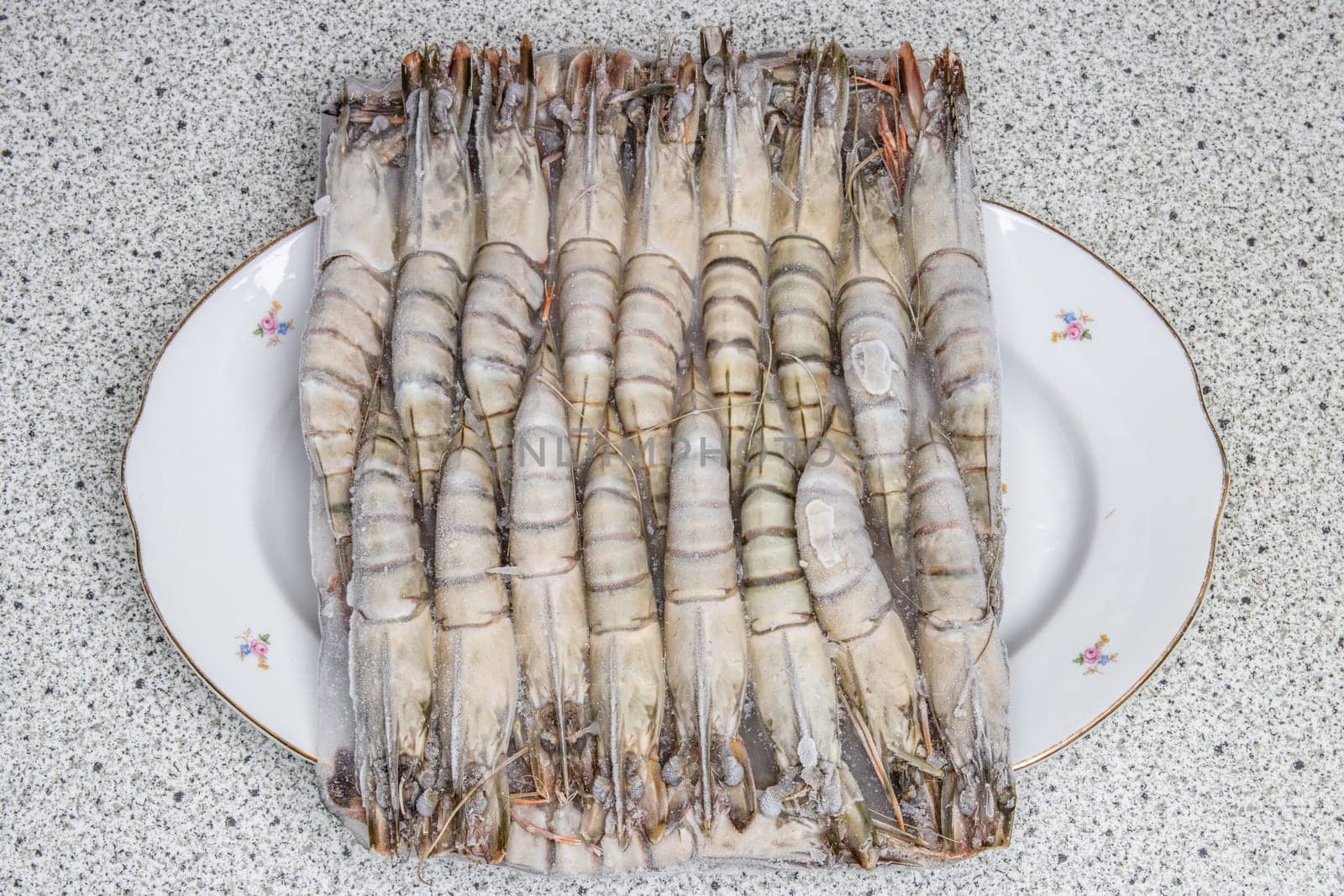 Frozen seafood background. Closeup of frozen fresh raw tiger shrimps on a plate. Top view. Concept healthy food.