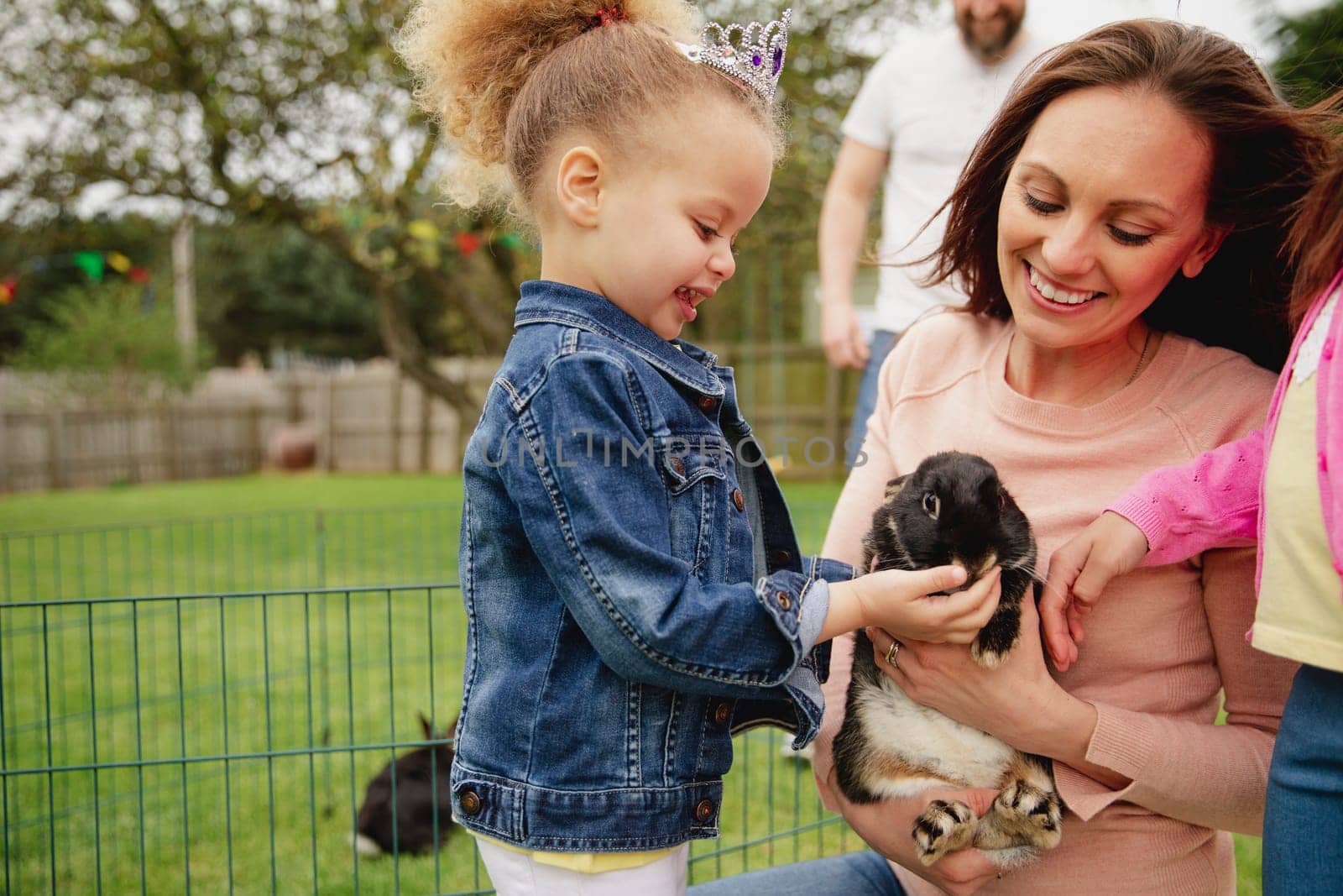 Little girl excited while stroking a pet rabbit ourdoors at a easter garden party.