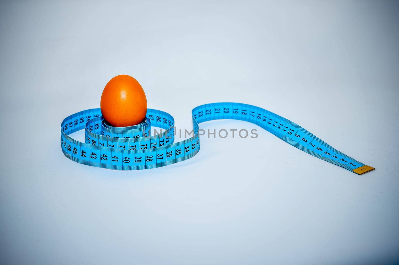 Egg wrapped in blue measuring tape, slimming concept.