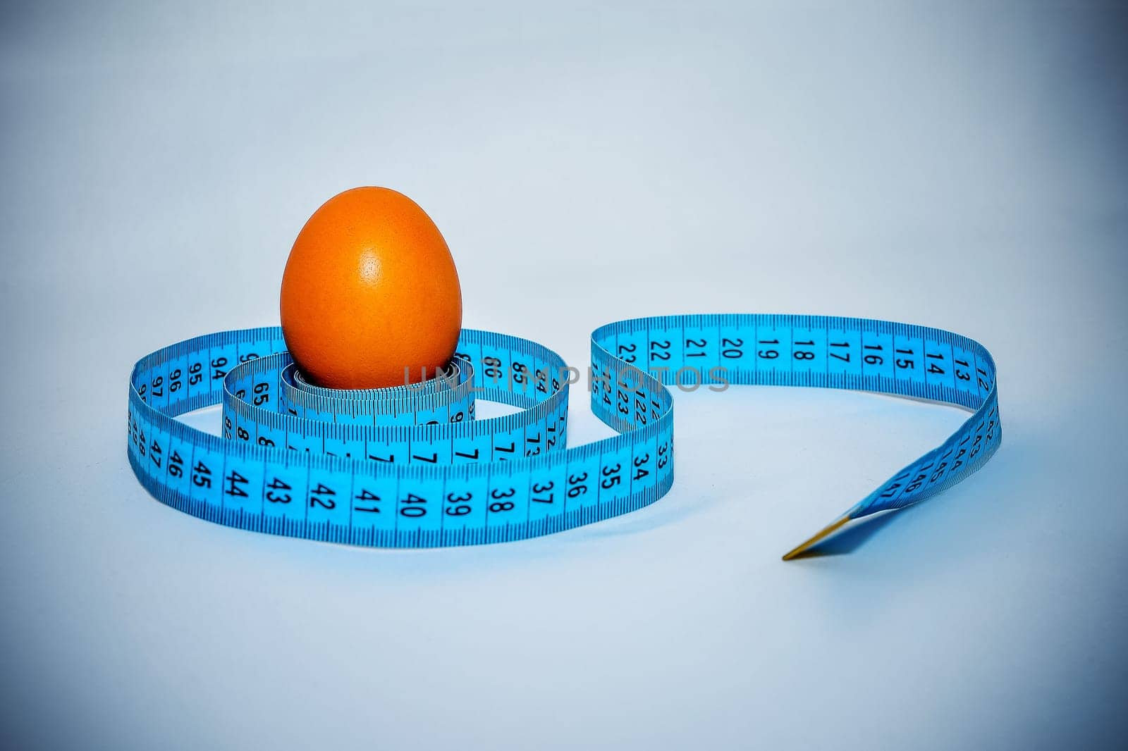 Egg wrapped in blue measuring tape, slimming concept.