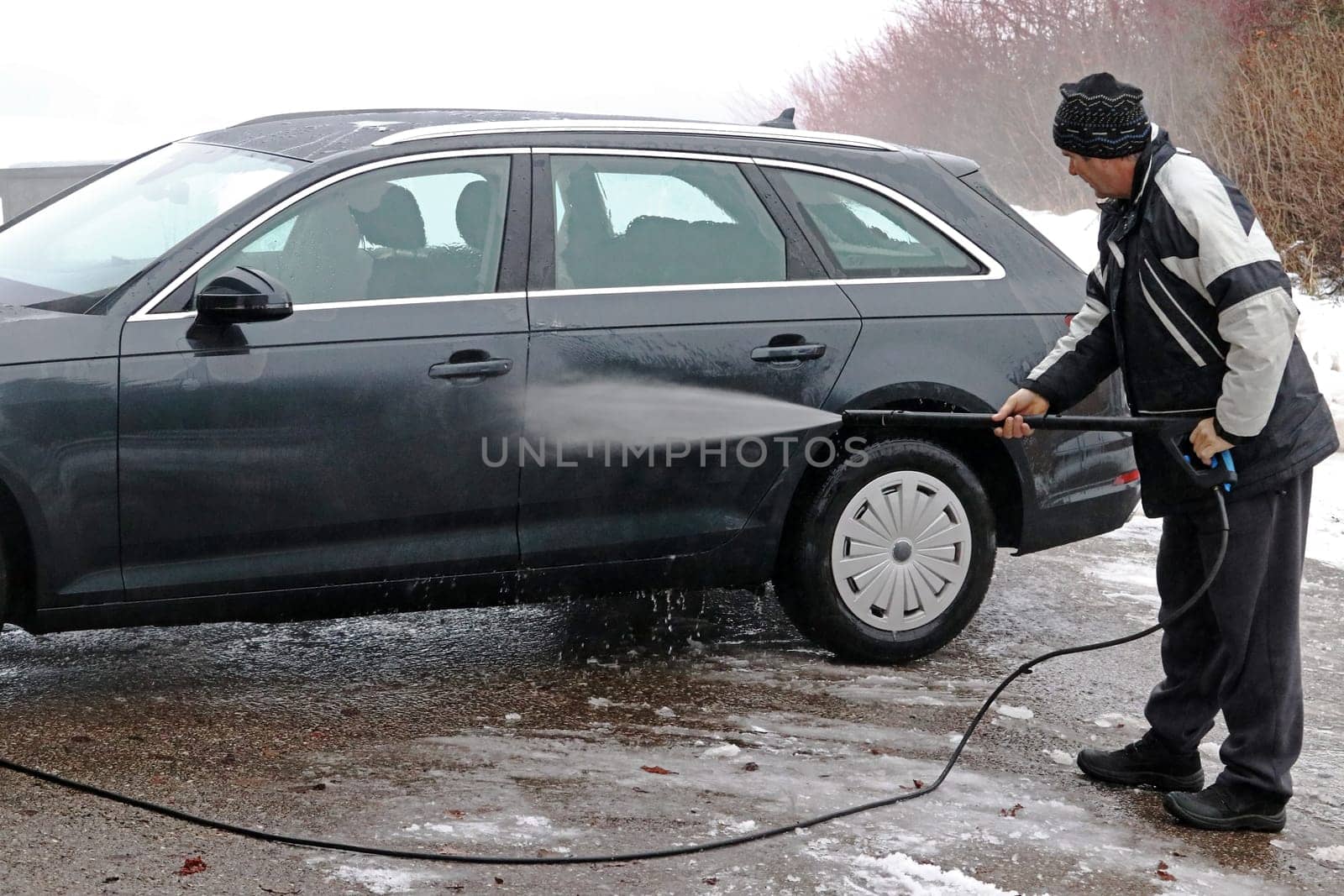 A man washes the dirt and salt off his car in winter.