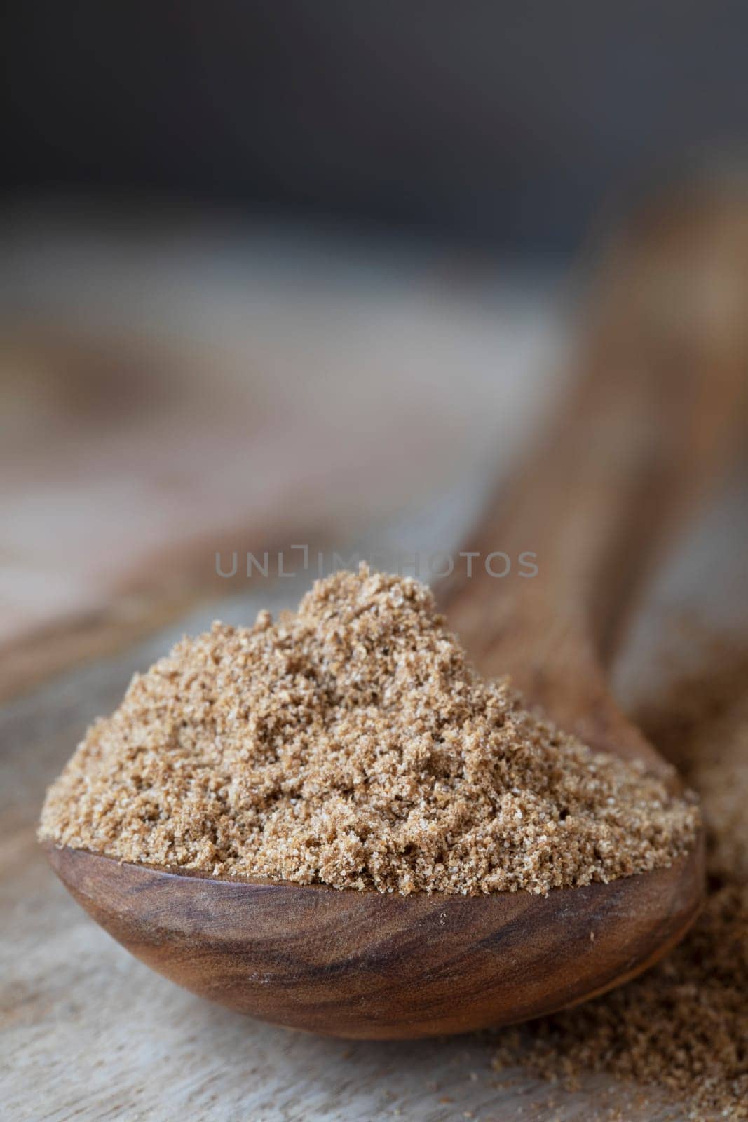 Ground coriander in wooden spoon, vertical with copy space