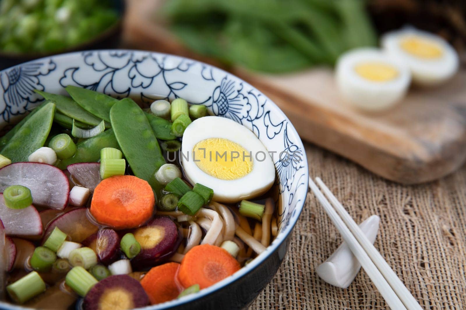 Colorful fresh bowl of udon noodle and vegetable soup with chopsticks.