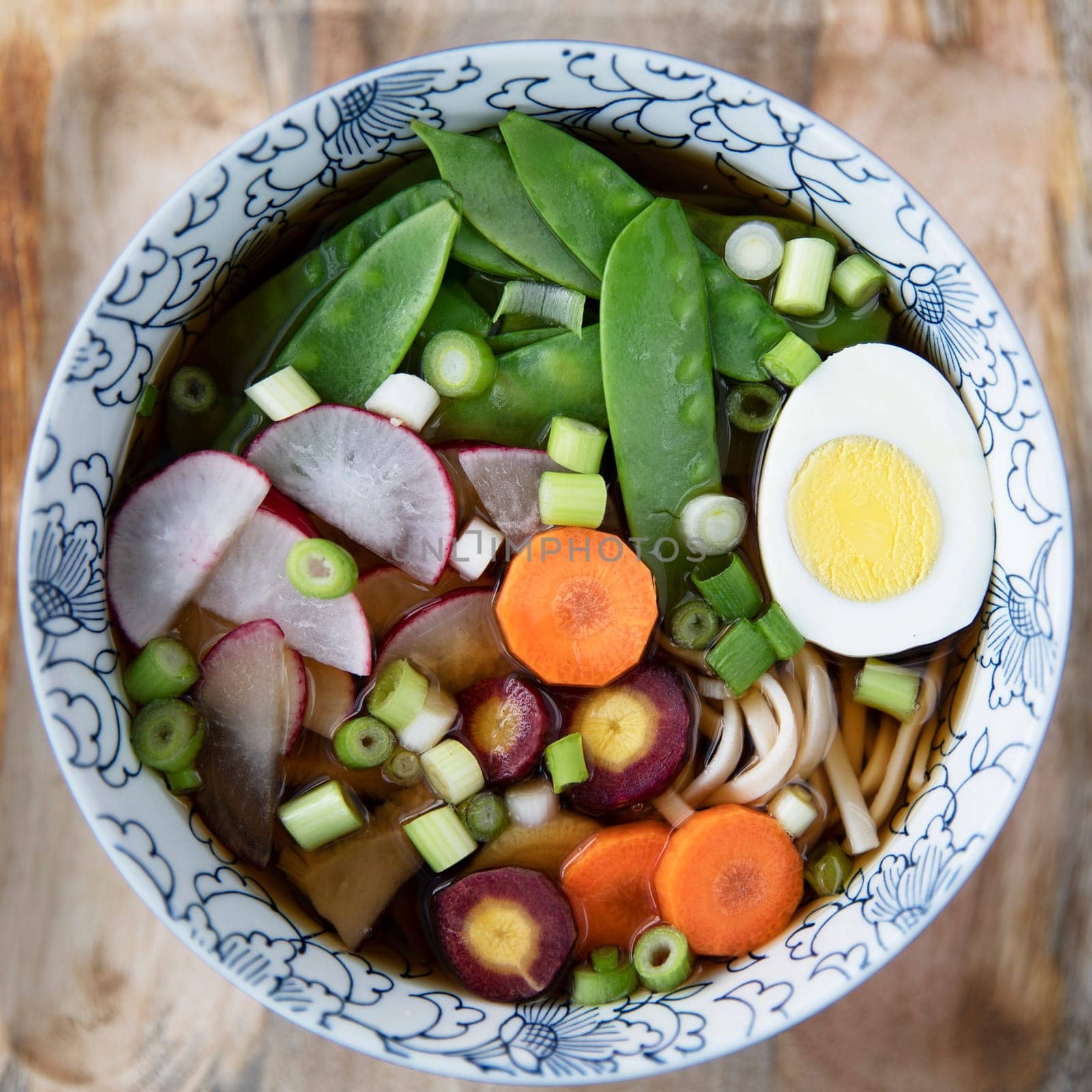 Colorful bowl of udon soup with fresh vegetables and hard boiled egg.  Flat lay, square format