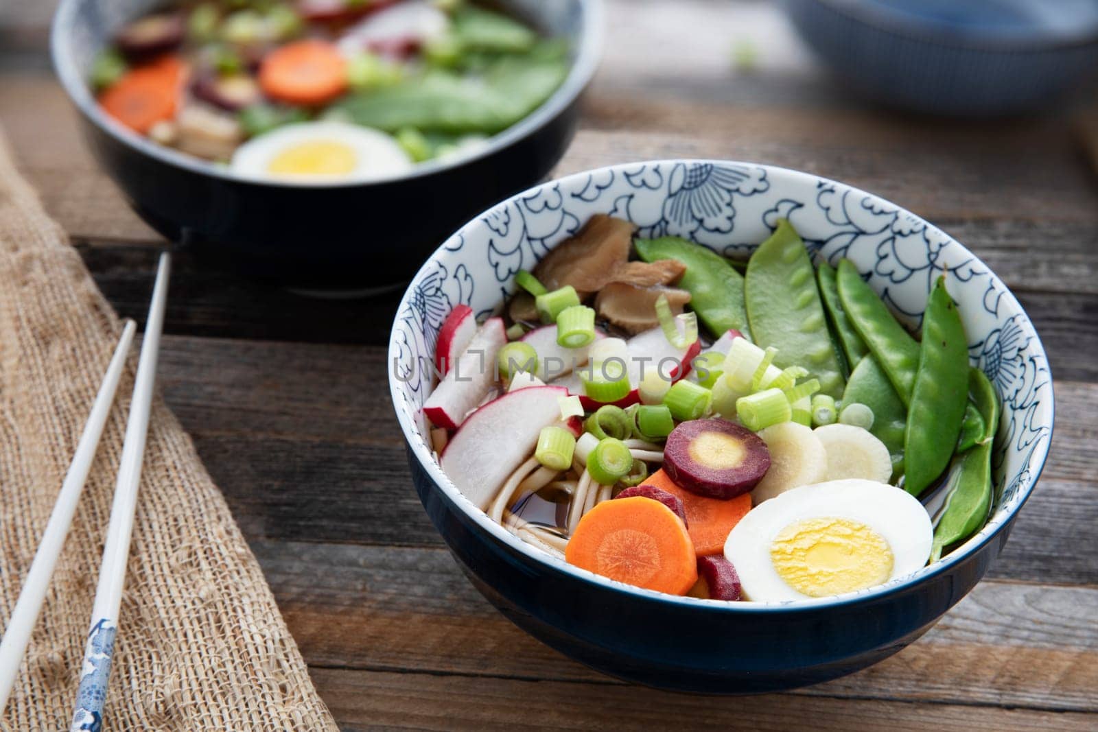 Colorful fresh bowl of udon noodle and vegetable soup with chopsticks.
